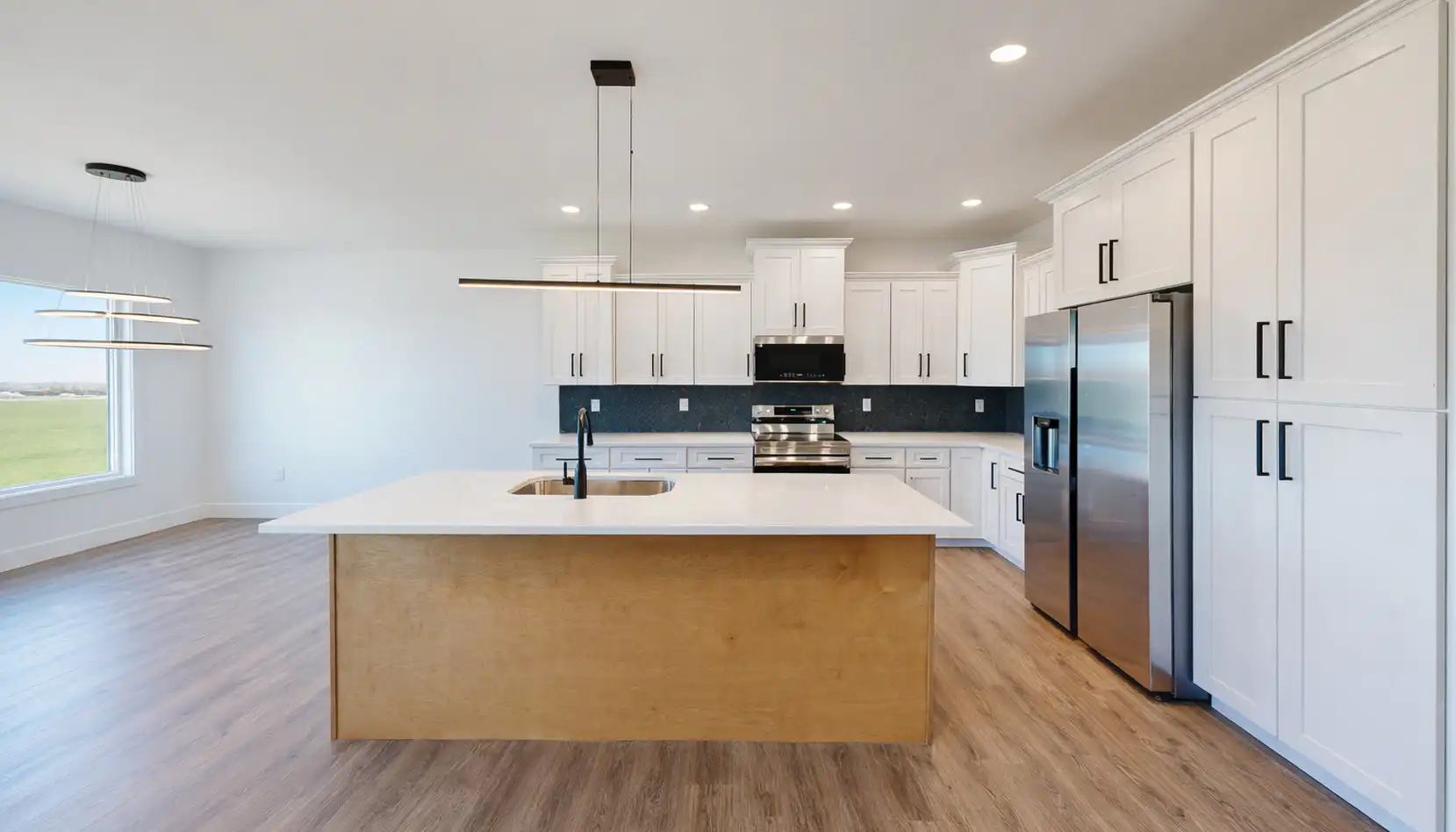 Modern kitchen with white cabinets, stainless steel appliances, a large central island with a sink, black backsplash, wood flooring, and pendant lighting. A large window provides natural light to the space, creating an inviting atmosphere perfect for any Leo who loves to entertain and shine in the heart of their home
