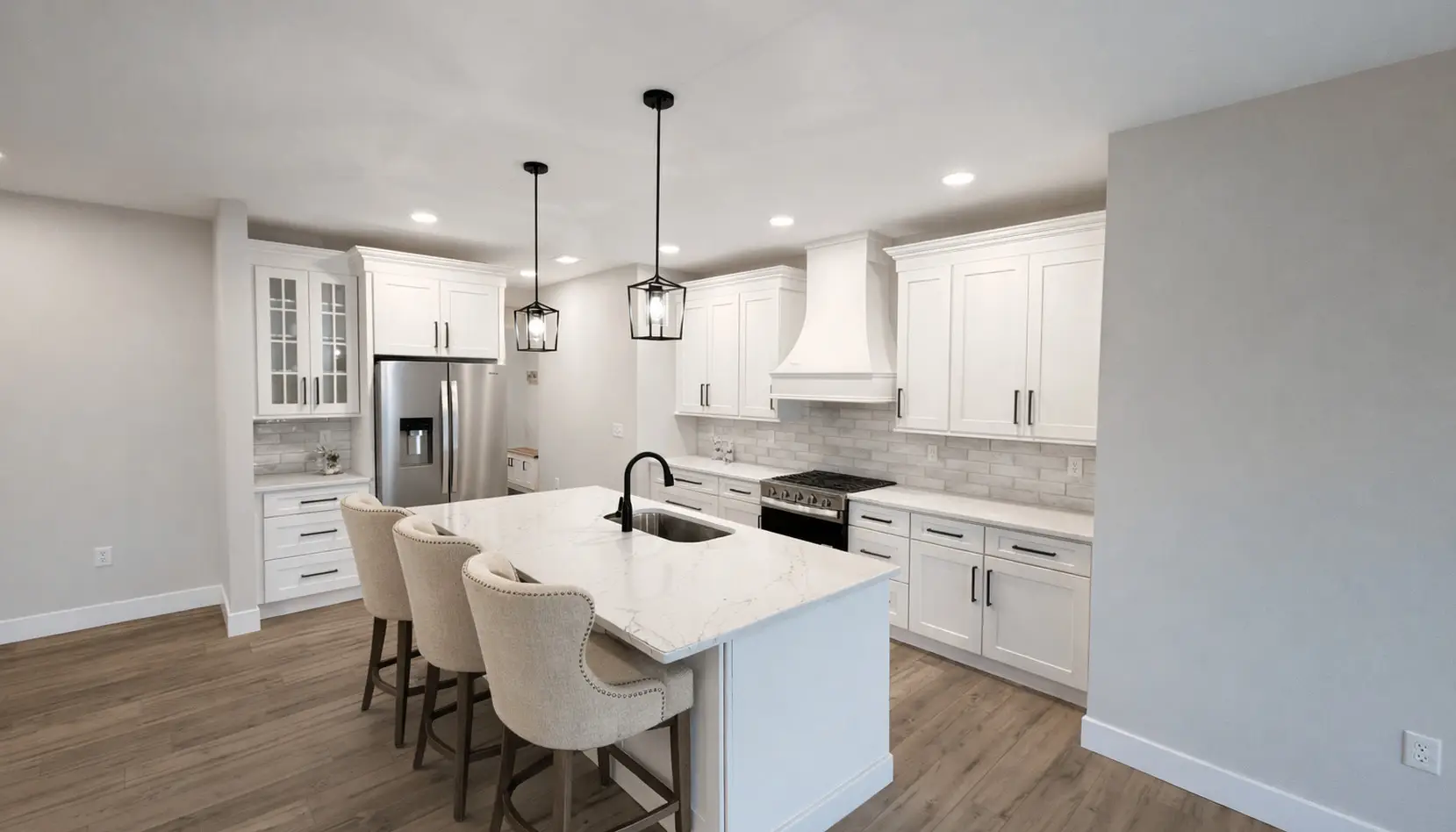 Modern Asher kitchen with white cabinets, marble island with three beige chairs, stainless steel appliances, pendant lights, and light wood flooring