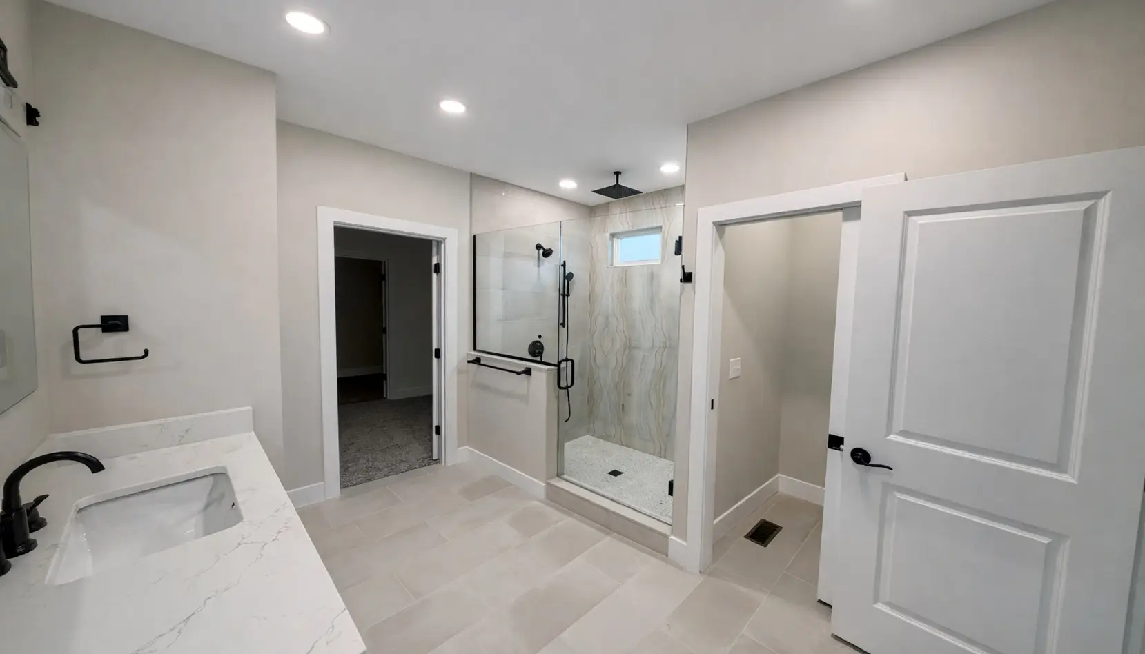Modern Asher bathroom with a glass-enclosed shower, double vanity featuring a white countertop, black fixtures, beige tile floor, and two white doors—one open to a separate toilet area