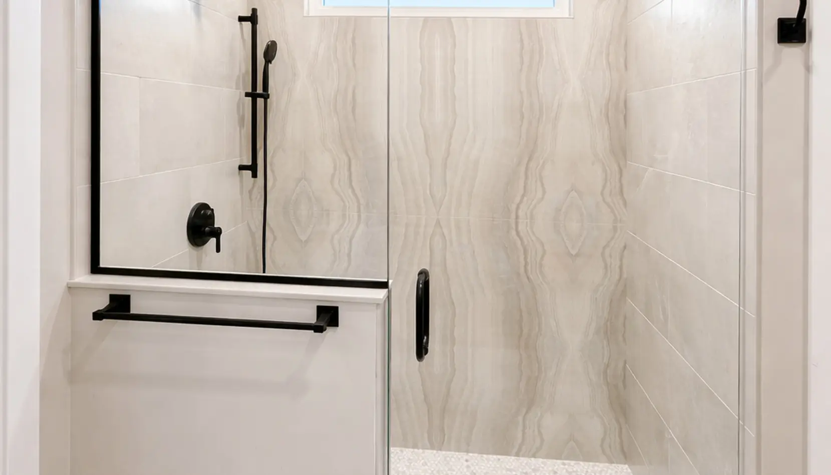 Modern Asher shower with glass door, black hardware, a black showerhead, and beige marble-patterned tiles on the walls. There is a towel bar on the door and a small window above the shower