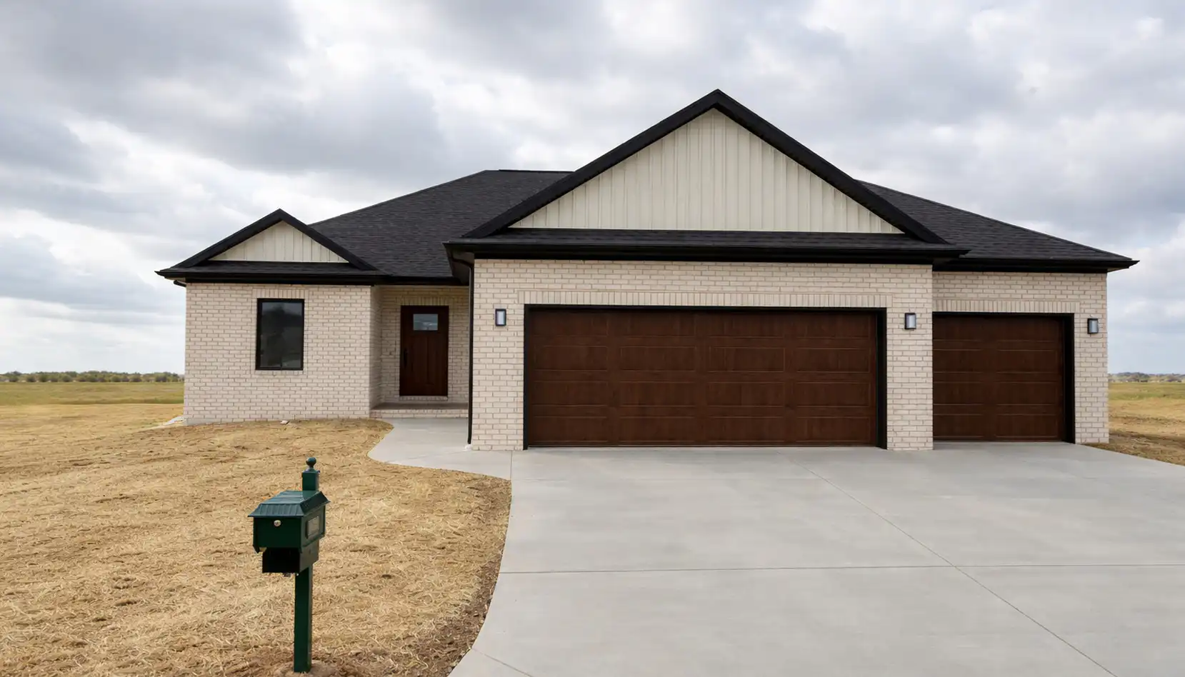 A modern single-story house with light brick exterior, dark roof, large brown garage doors, and a green mailbox at the edge of a concrete driveway sits surrounded by dry grass beneath a cloudy sky—an inviting home perfectly suited for a Leo seeking both style and comfort