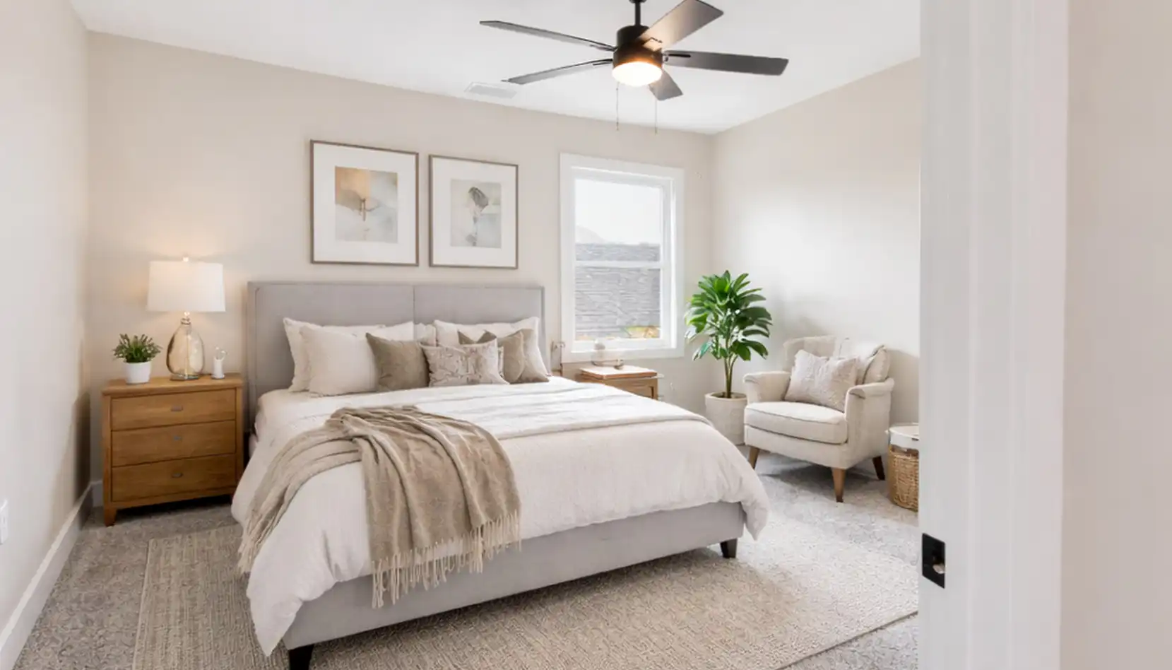 Bright bedroom with a large bed featuring a DaVinci-inspired gray upholstered headboard, beige bedding, two wooden nightstands, lamps, framed art, an armchair, a potted plant, and a ceiling fan