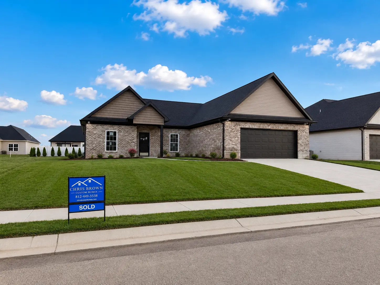 A single-story brick house with a dark roof and two-car garage sits on a manicured lawn in the desirable Kirkwood neighborhood. A SOLD sign from Chris Brown Realty is displayed in front, with a bright blue sky and clouds overhead