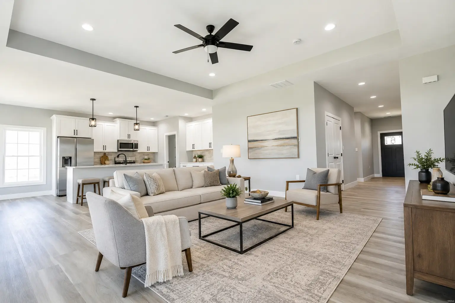 Modern open-concept living room and kitchen in Kirkwood with neutral tones, gray sofa, two armchairs, coffee table, ceiling fan, and minimalist decor on light wood flooring
