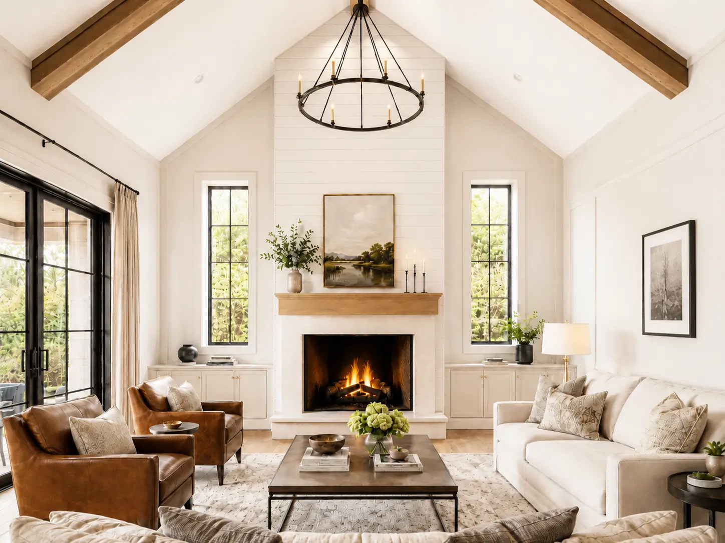 Bright living room with vaulted ceiling, fireplace, two brown Theo chairs, white sofa, large windows, chandelier, coffee table with flowers, and neutral decor