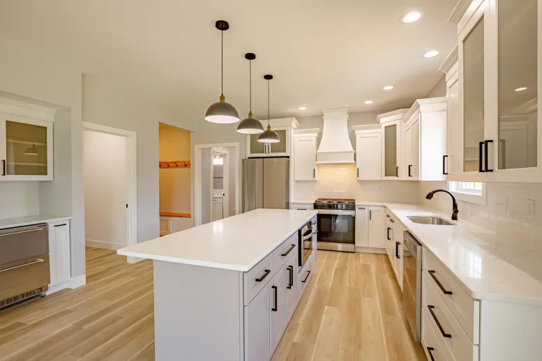 Modern kitchen with white cabinets, light wood floors, a large island, black pendant lights, stainless steel appliances, and bright recessed lighting—perfect inspiration for your next home decor blog.