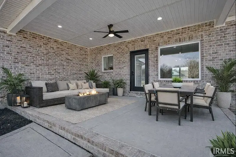 Covered patio in the Ava floor plan with sofa, fire pit table, dining set, and ceiling fan.