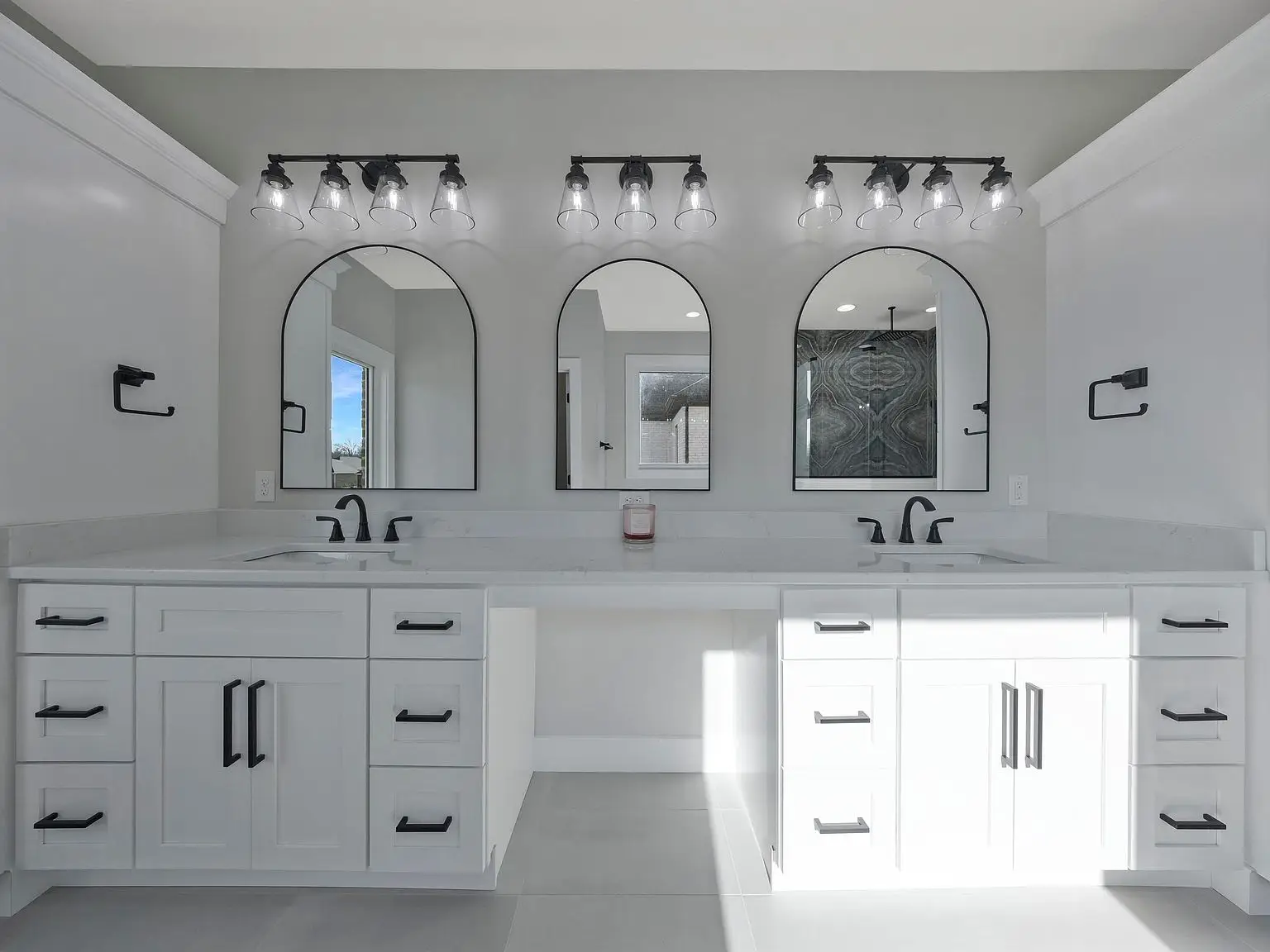 Modern bathroom in the Ava floor plan with double sinks, black fixtures, and arched mirrors.