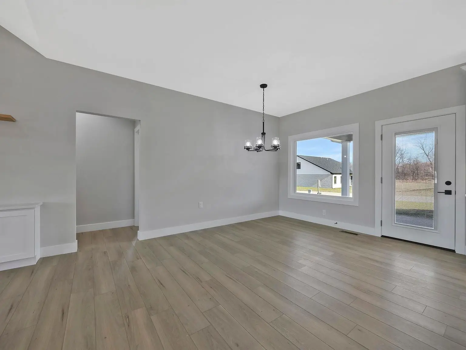Empty room in the Ava floor plan with light wood floors, gray walls, and modern black chandelier.