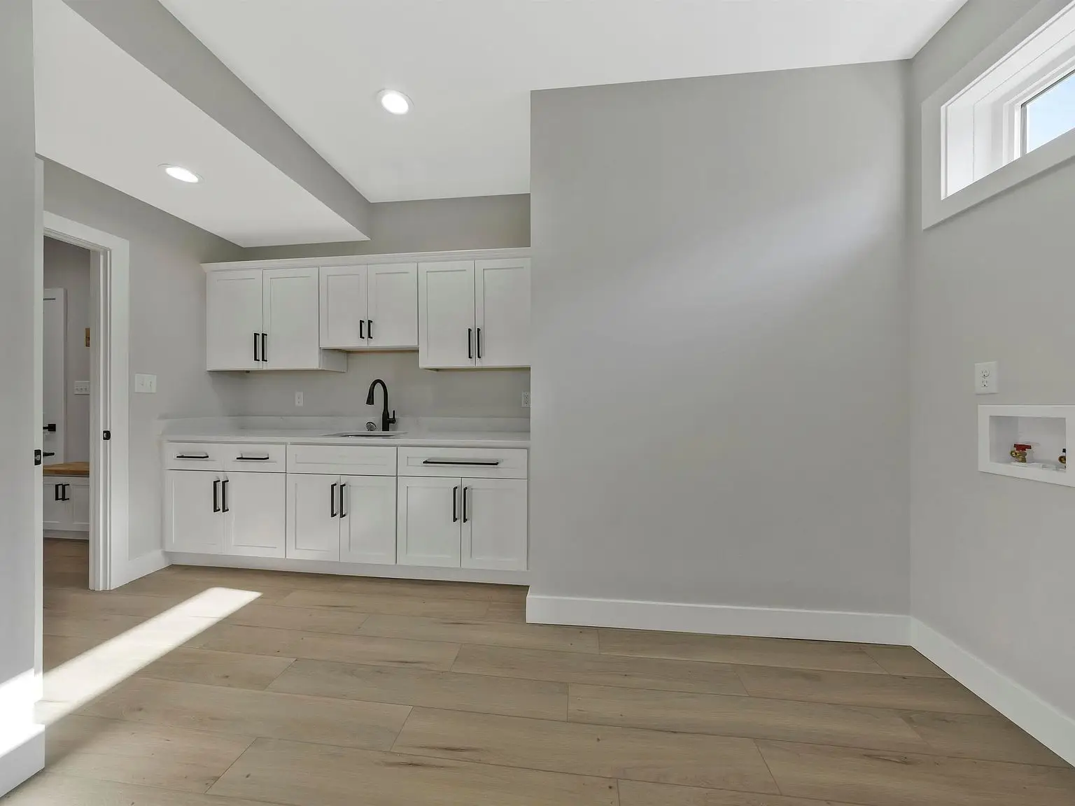 Laundry room in the Ava floor plan with white cabinets, wood floors, and bright lighting.