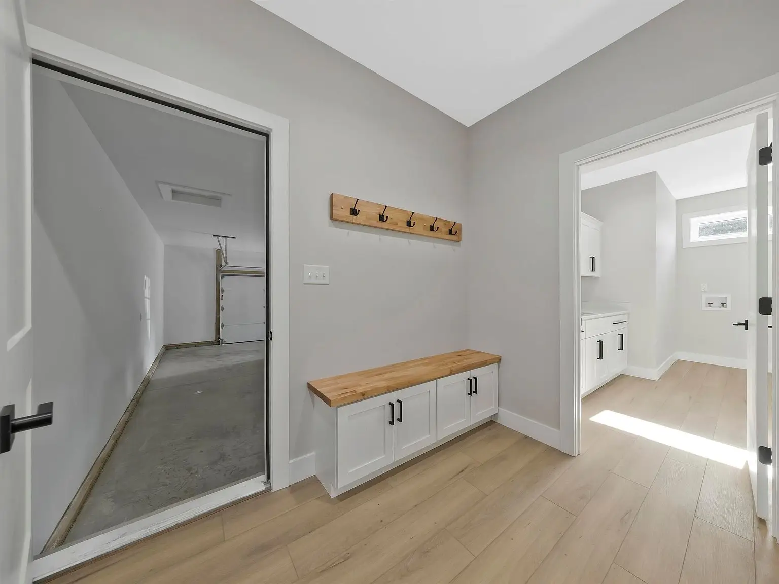 Room with wood bench, coat hooks, light wood floor, and door to garage in the Ava floor plan.