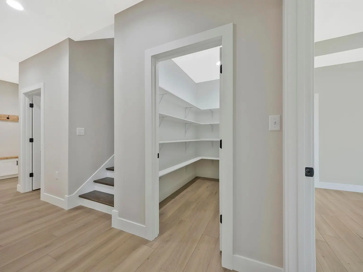 Open pantry in the Ava floor plan with white shelves, wood floor, and gray walls by staircase.