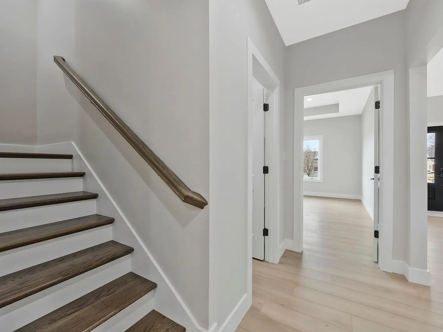 A hallway with light wood floors, white walls, and an Ava staircase by Chris Brown Homes.
