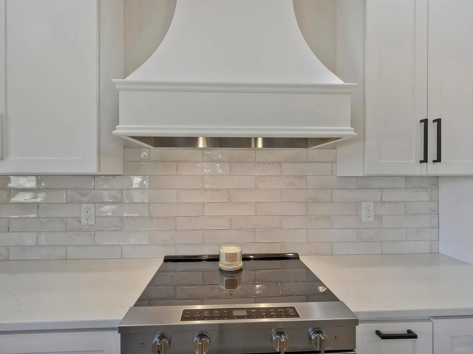 A modern kitchen stove with a candle on top, white cabinets, and the Ava floor plan’s backsplash.