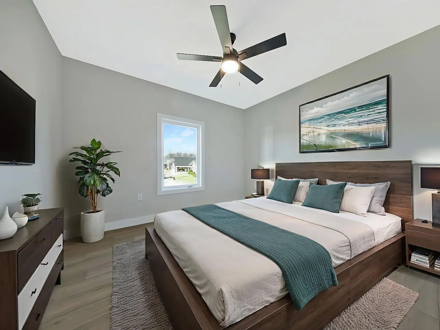 Modern bedroom in the Ava floor plan with large bed, ceiling fan, TV, and a potted plant.