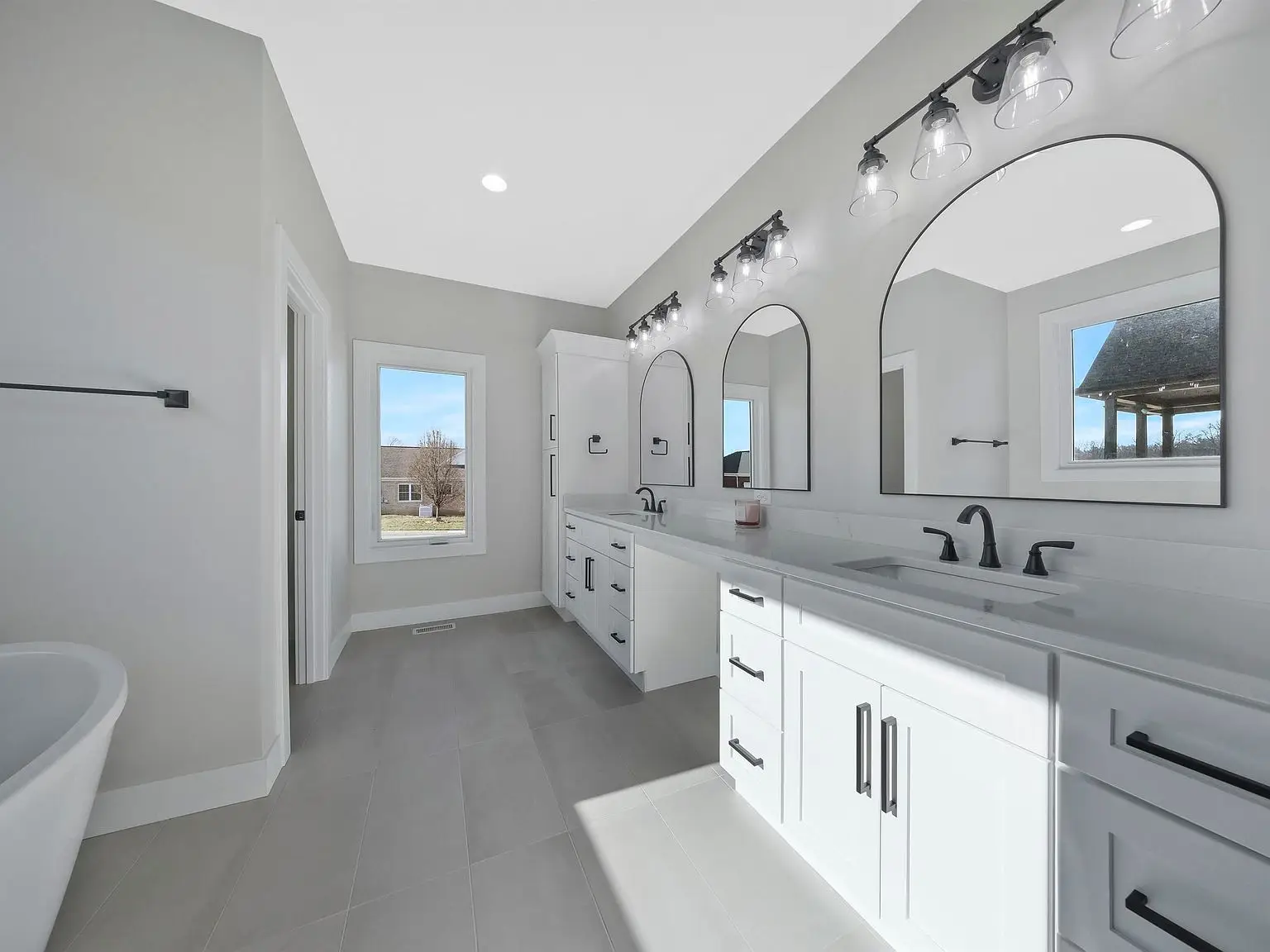 Modern bathroom in the Ava floor plan with double sinks, arched mirrors, and natural light.