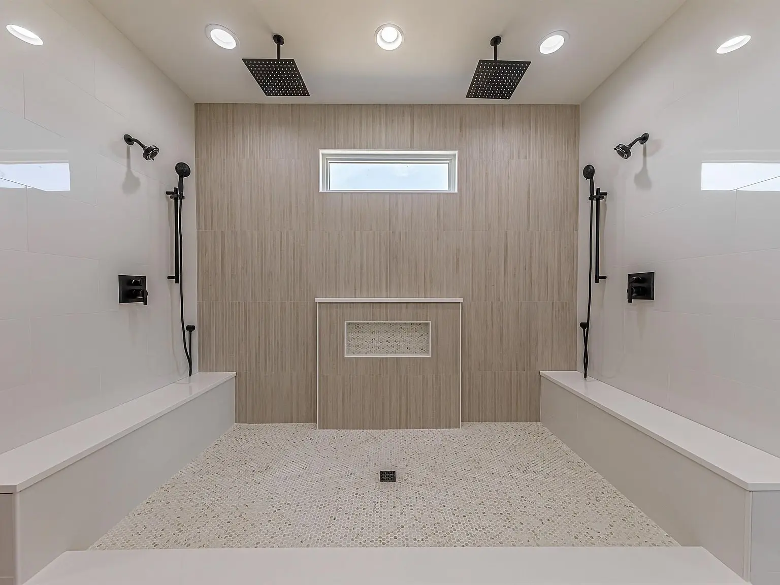 Spacious DaVinci double shower with two benches, dual showers, and window above tiled wall.