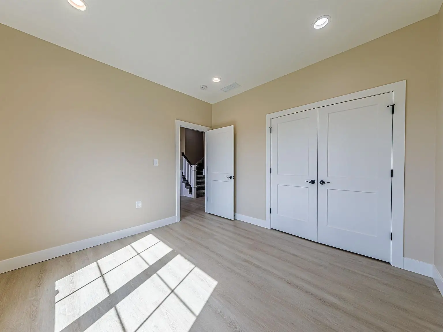 Empty beige room with wood floor, DaVinci floor plan, double closets, and sunlight on floor.
