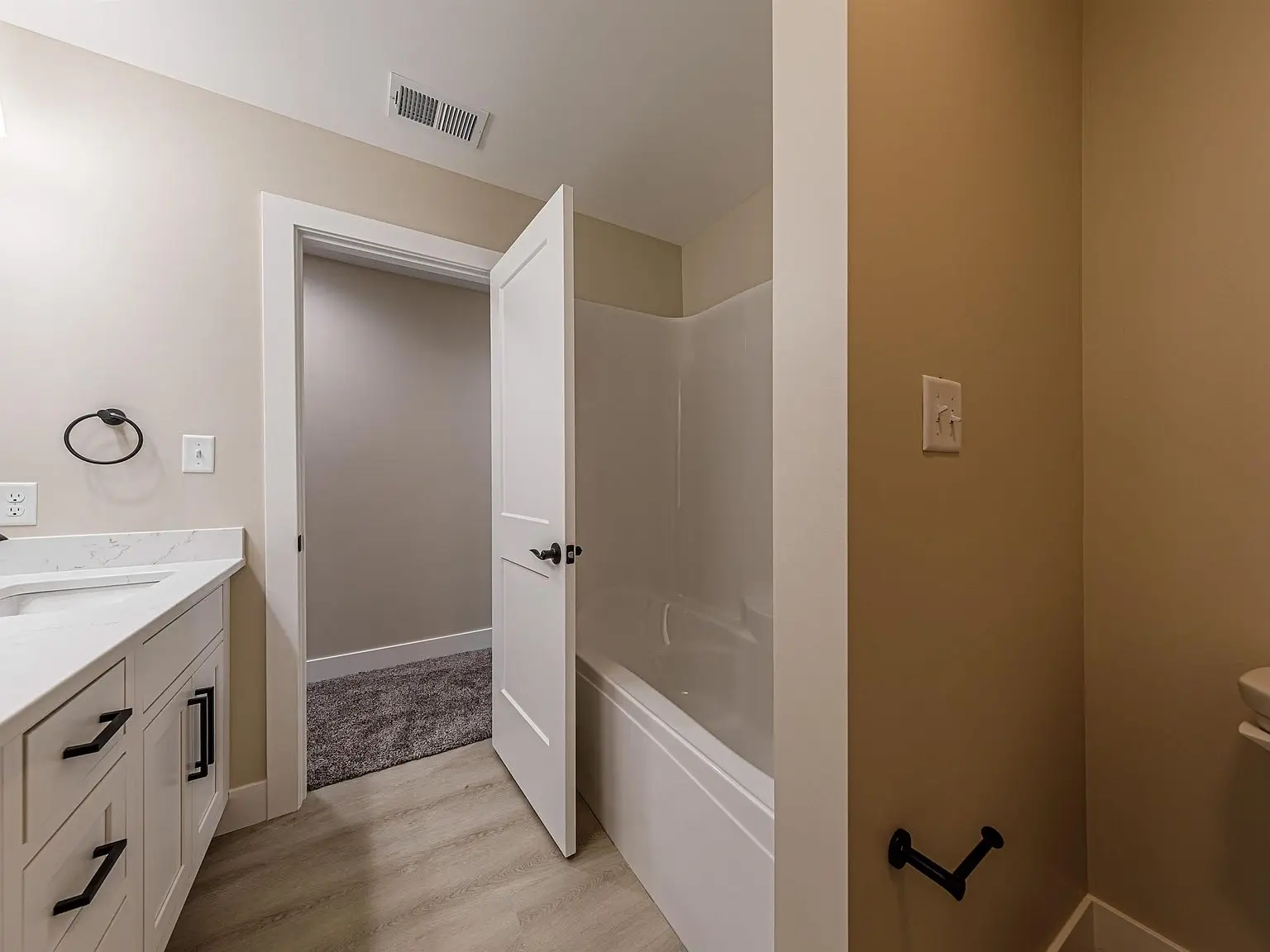 Bathroom with a white vanity, DaVinci floor plan, open door, bathtub, and beige walls.