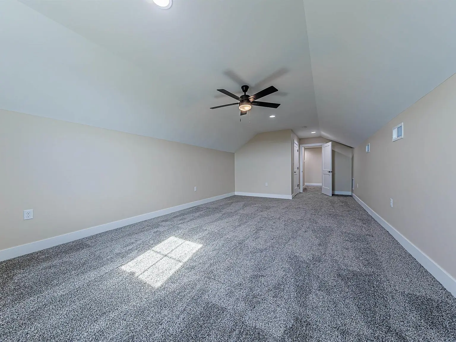 Spacious DaVinci floor plan: empty carpeted room with sloped ceiling, fan, and hallway entrance.