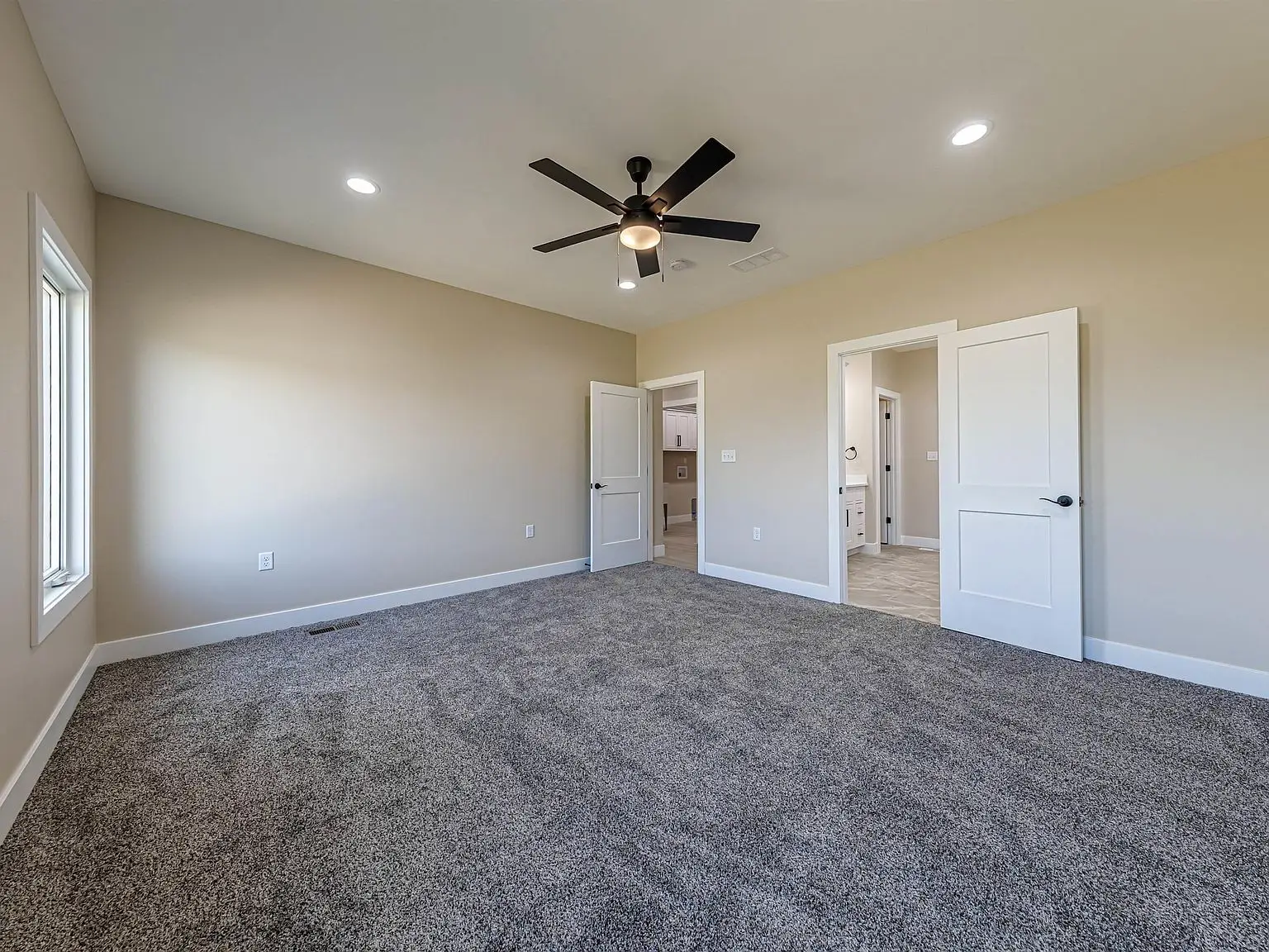 Empty carpeted room in the DaVinci floor plan with beige walls, ceiling fan, and open doors.