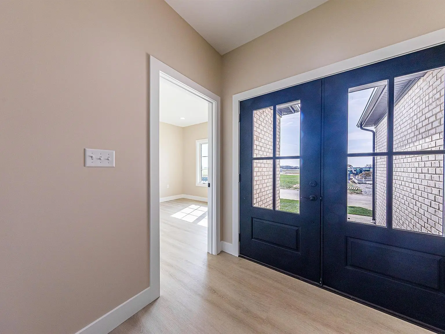 Entryway with black double doors, showcasing DaVinci floor plan wood flooring in a bright room.