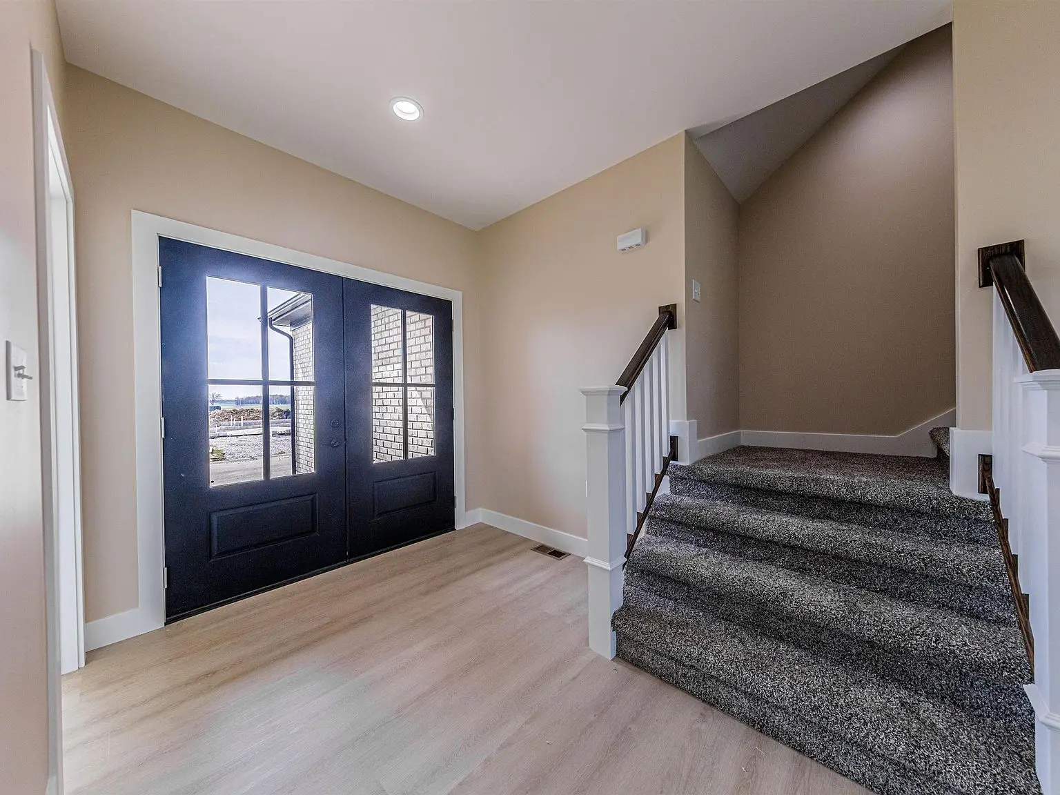 Entryway in the DaVinci floor plan: double doors, beige walls, wood floor, carpeted stairs.