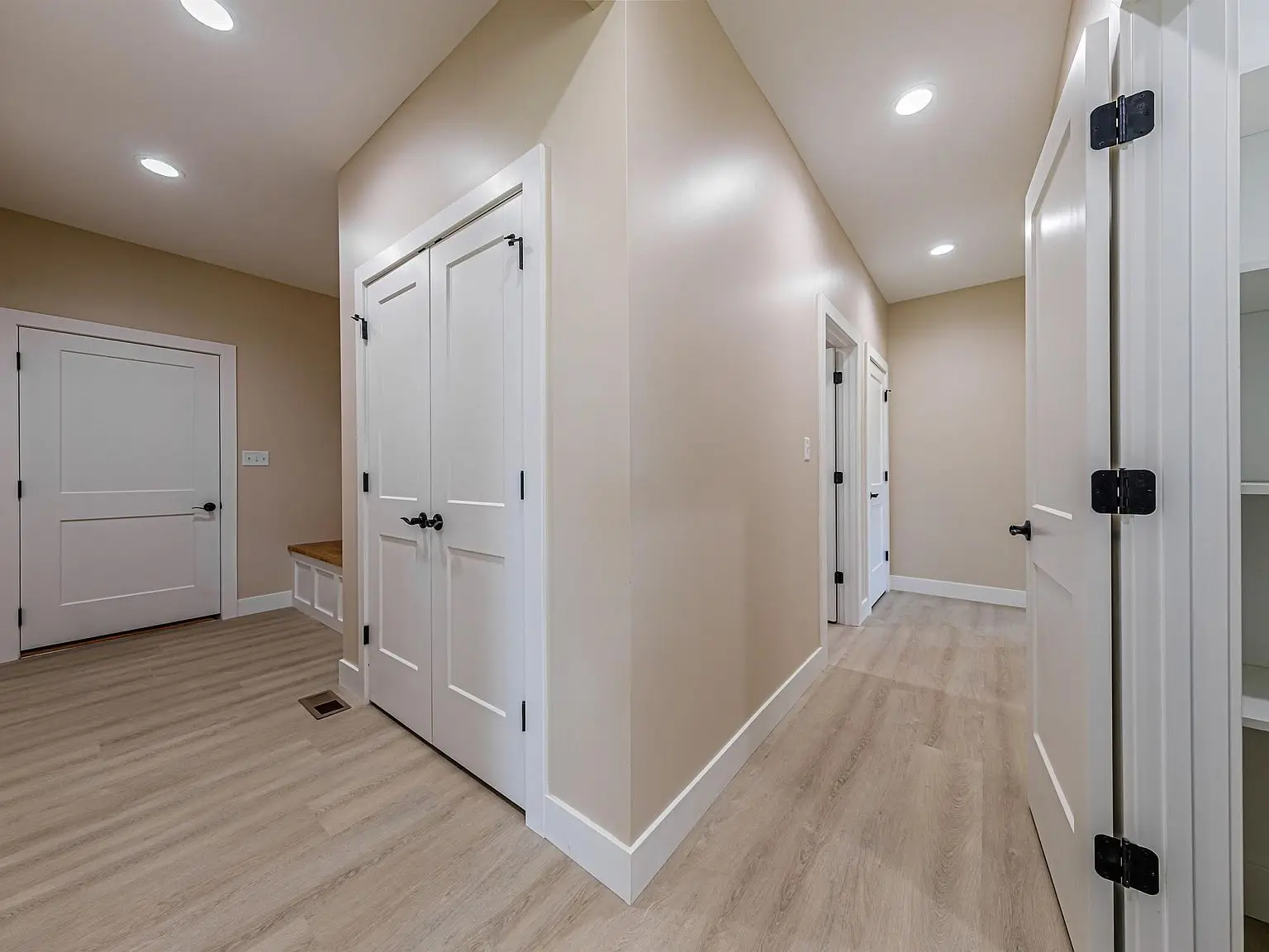 A hallway in the DaVinci floor plan with light wood floors, beige walls, and white doors.