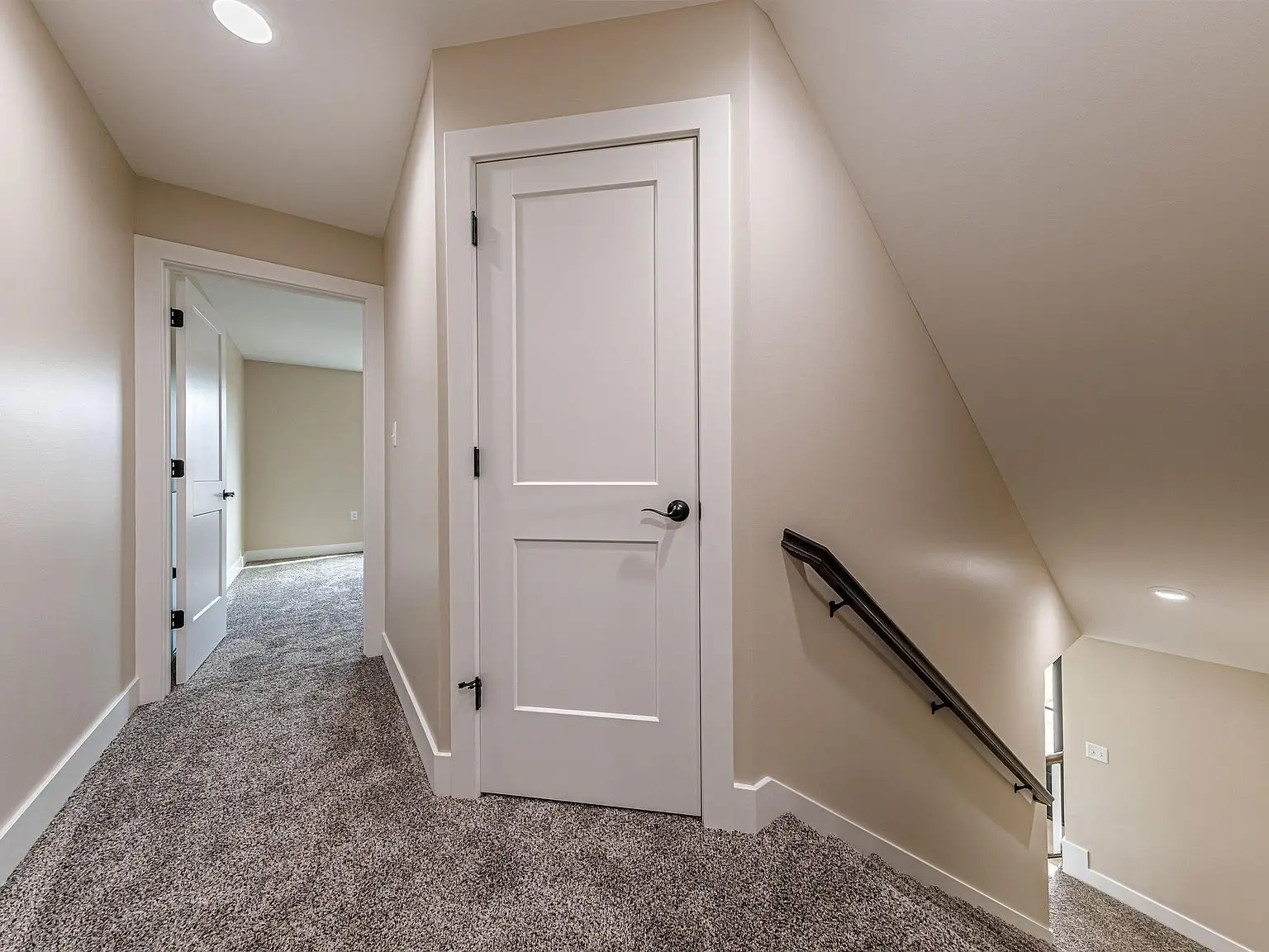 Hallway with beige walls, carpeted floor, and DaVinci floor plan stairs with handrail.