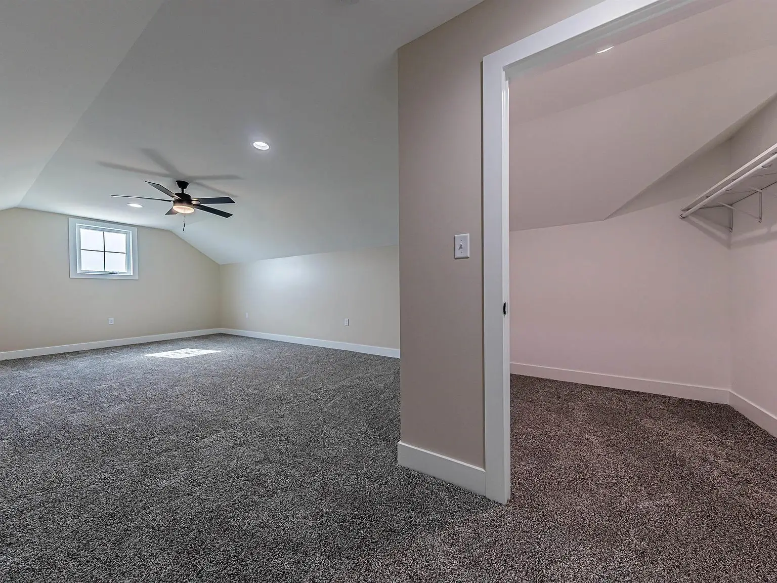 Carpeted room in the DaVinci floor plan with sloped ceiling, fan, window, and open closet.