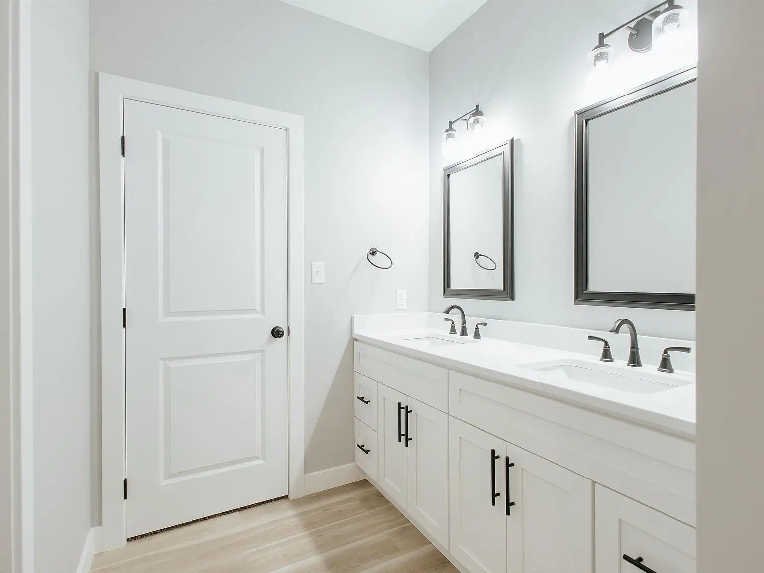White bathroom with double sink vanity, mirrors, and closed door—part of the Eleanor floor plan.