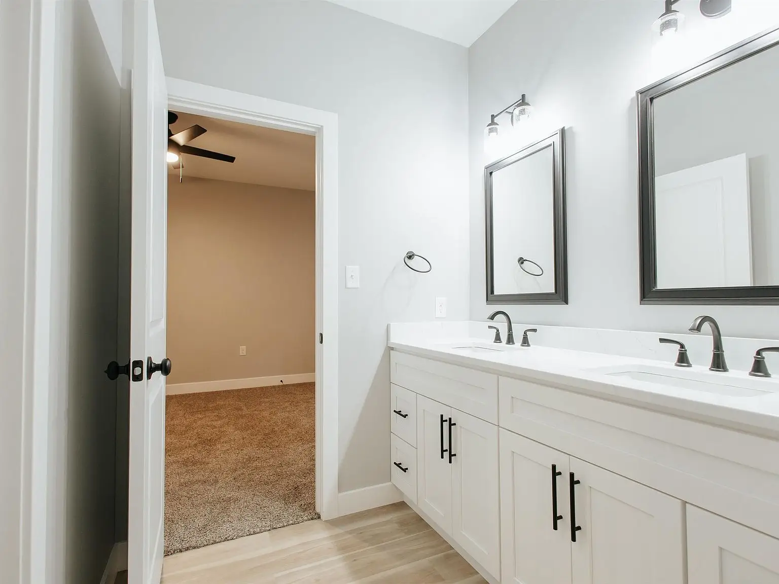 A bathroom in the Eleanor floor plan features double sinks, white cabinets, and a carpeted view.