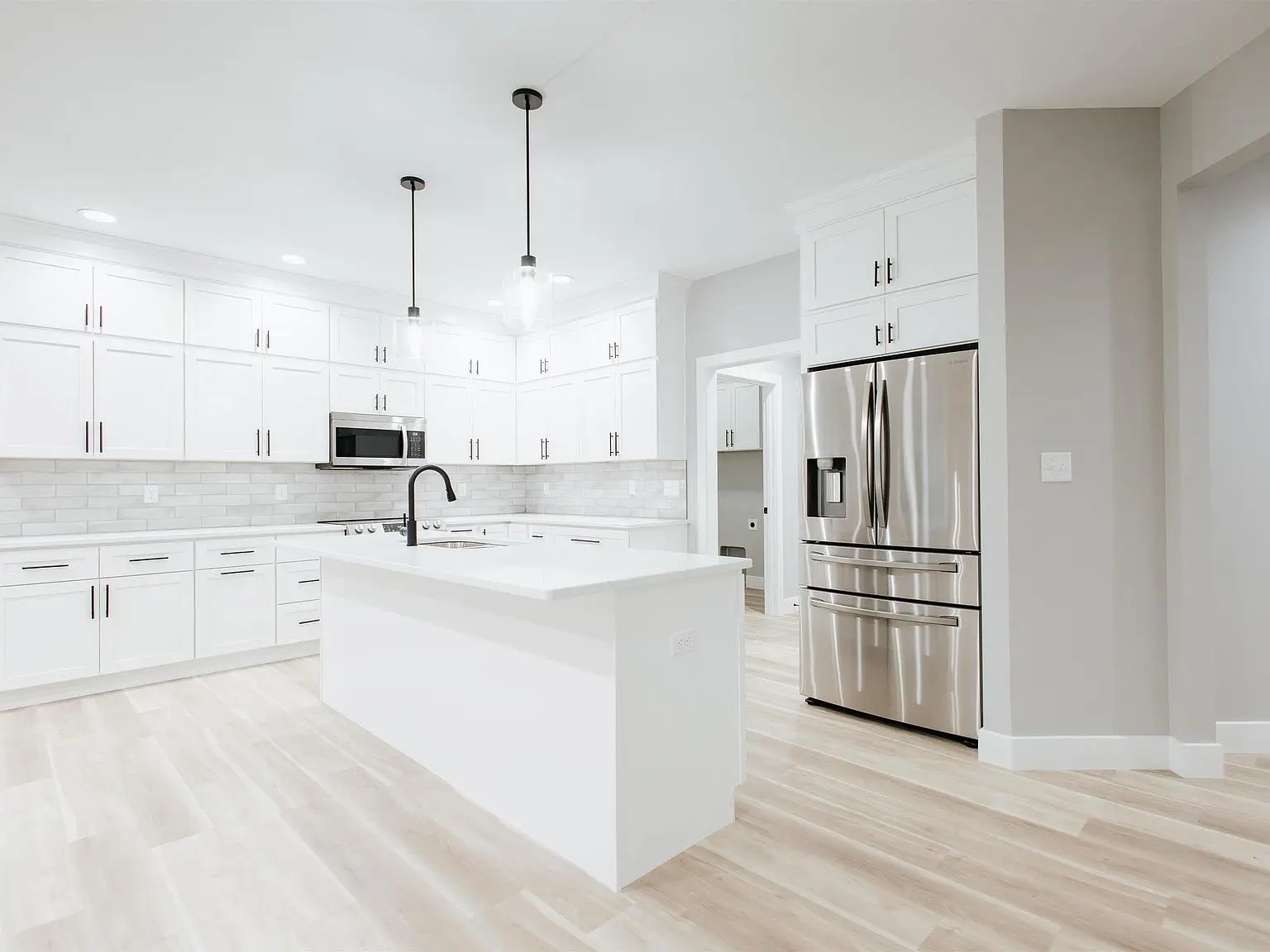 Modern kitchen in the Eleanor floor plan with white cabinets and light wood flooring.