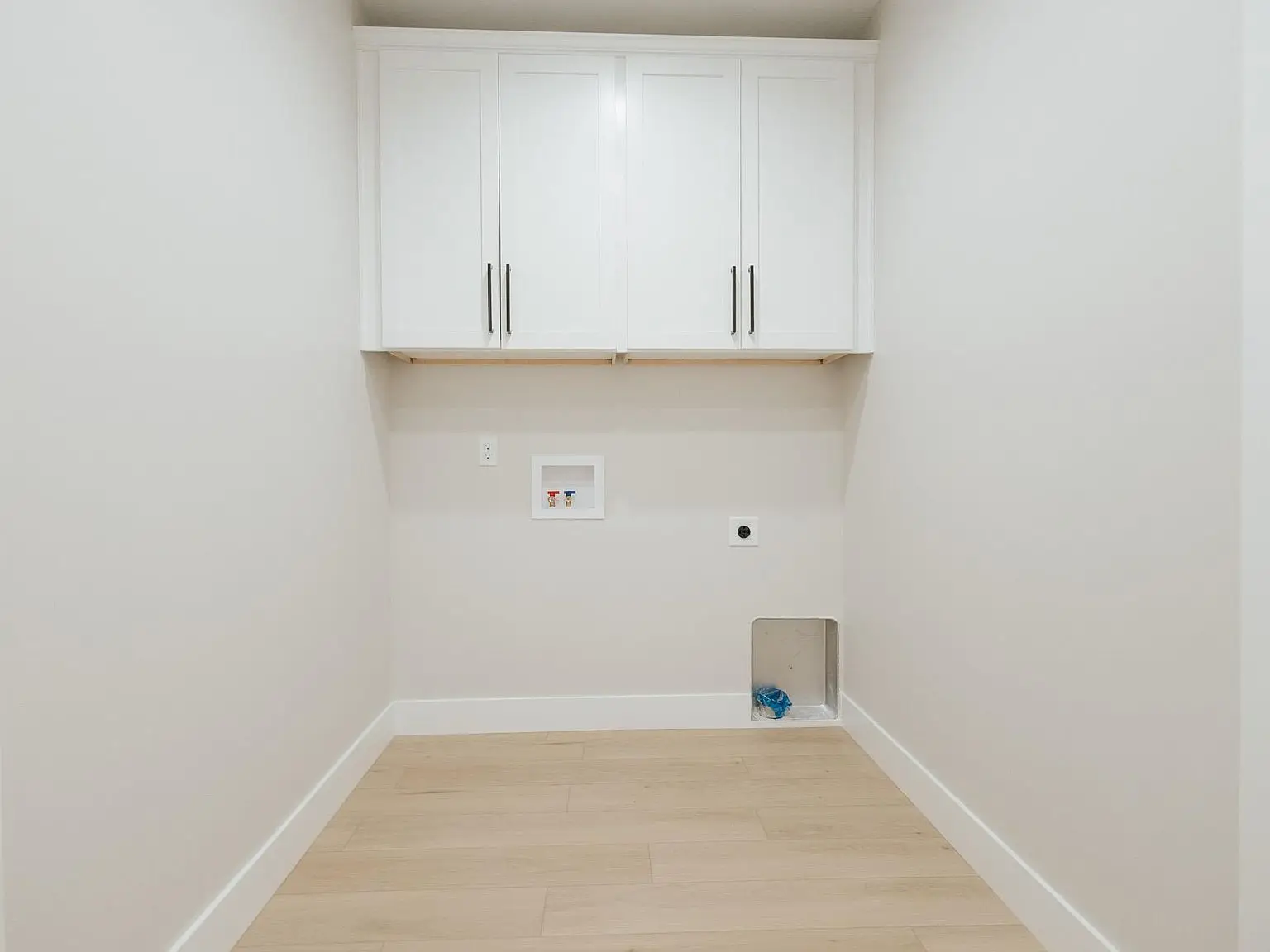 Empty laundry room with white cabinets, hookups, wood flooring in the Harper home floor plan.