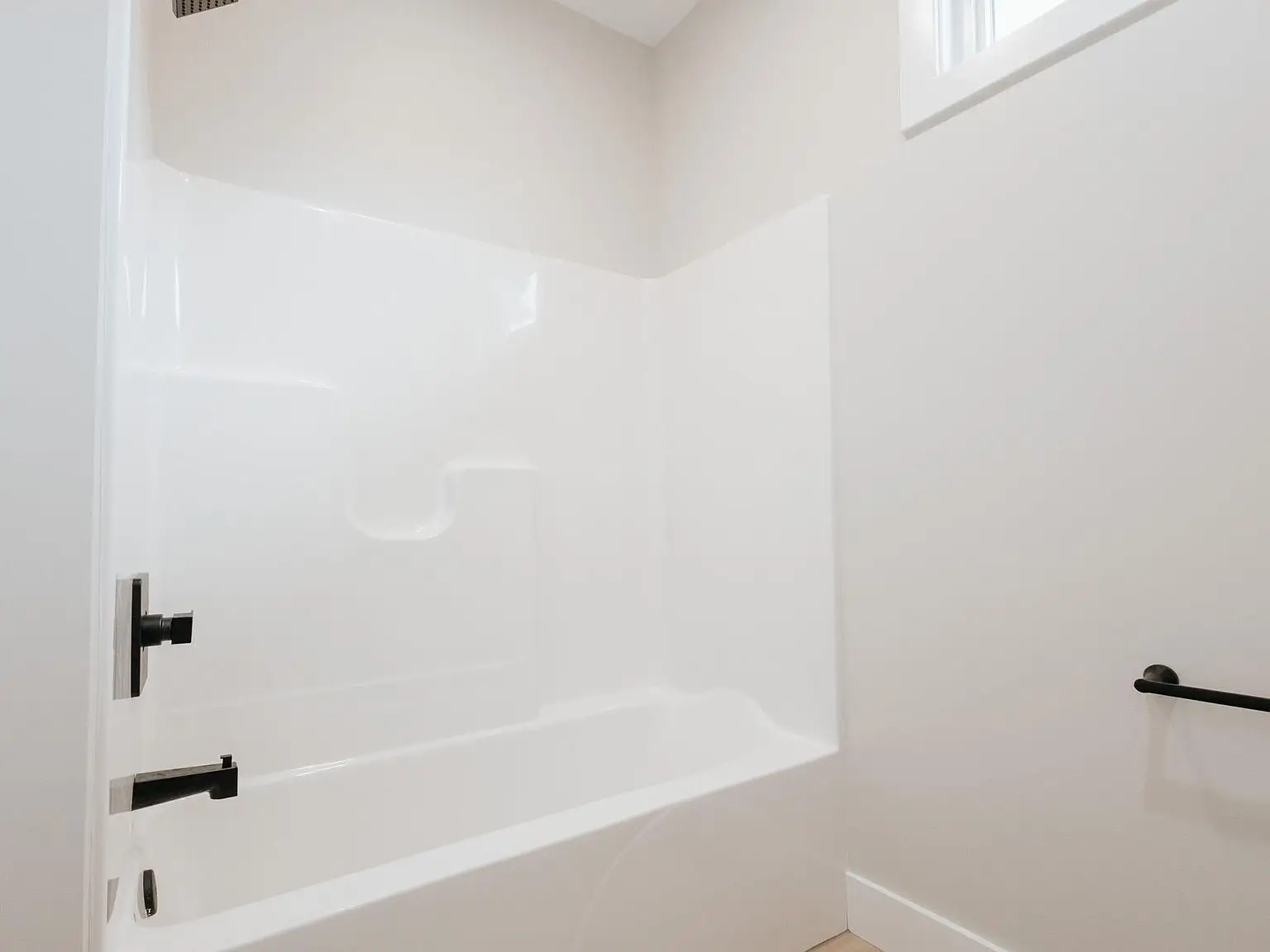 Minimal, light-colored bathroom in the Harper home with white tub and sleek black fixtures.