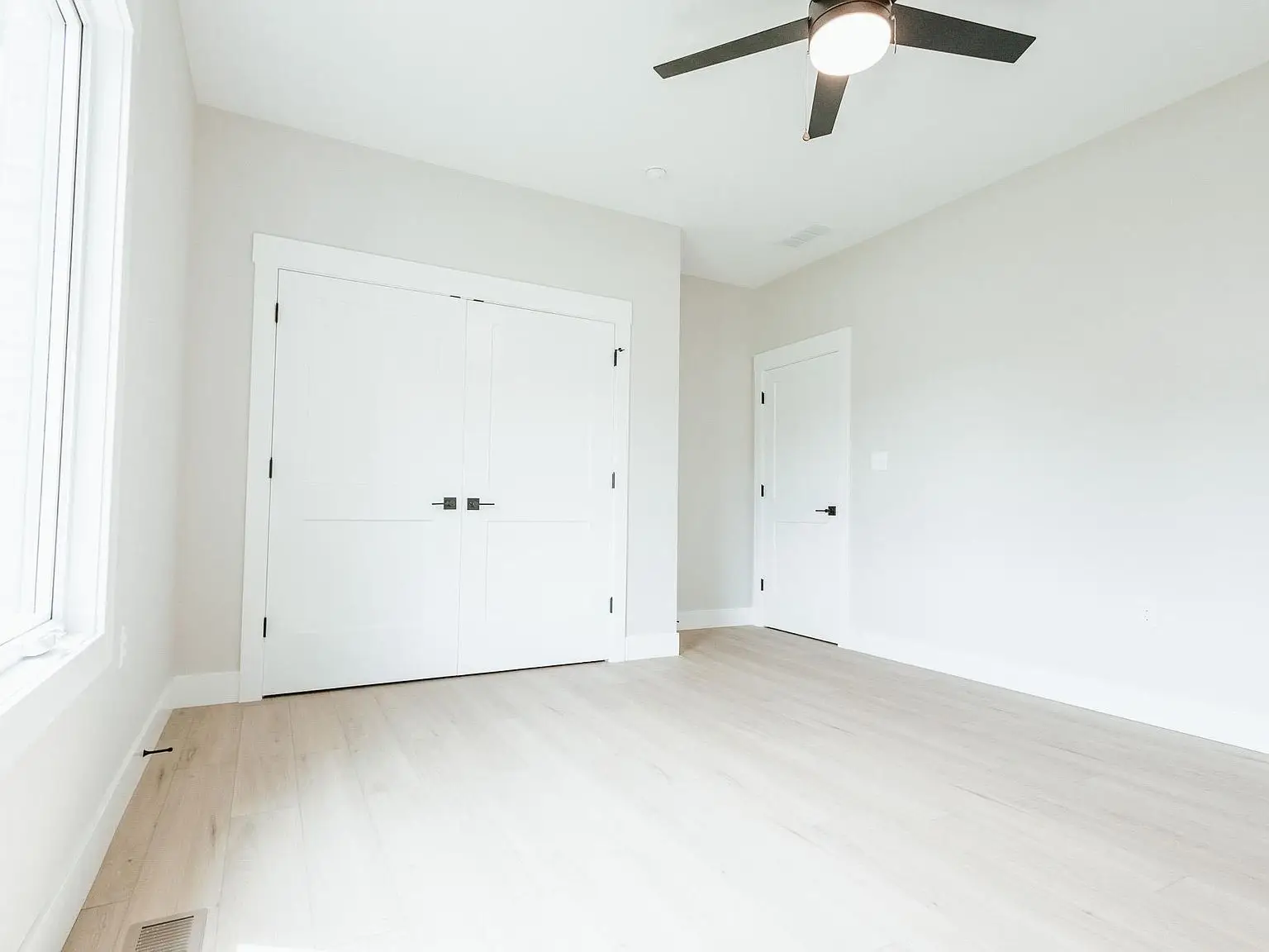Empty, bright Harper home with light wood floors, white walls, and a ceiling fan above.