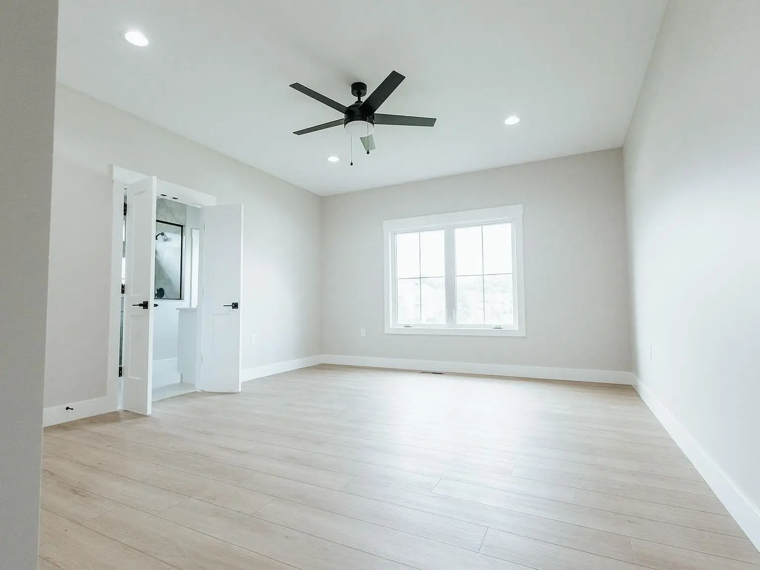 Empty Harper floor plan room with light wood floors, white walls, fan, window, and bath door.