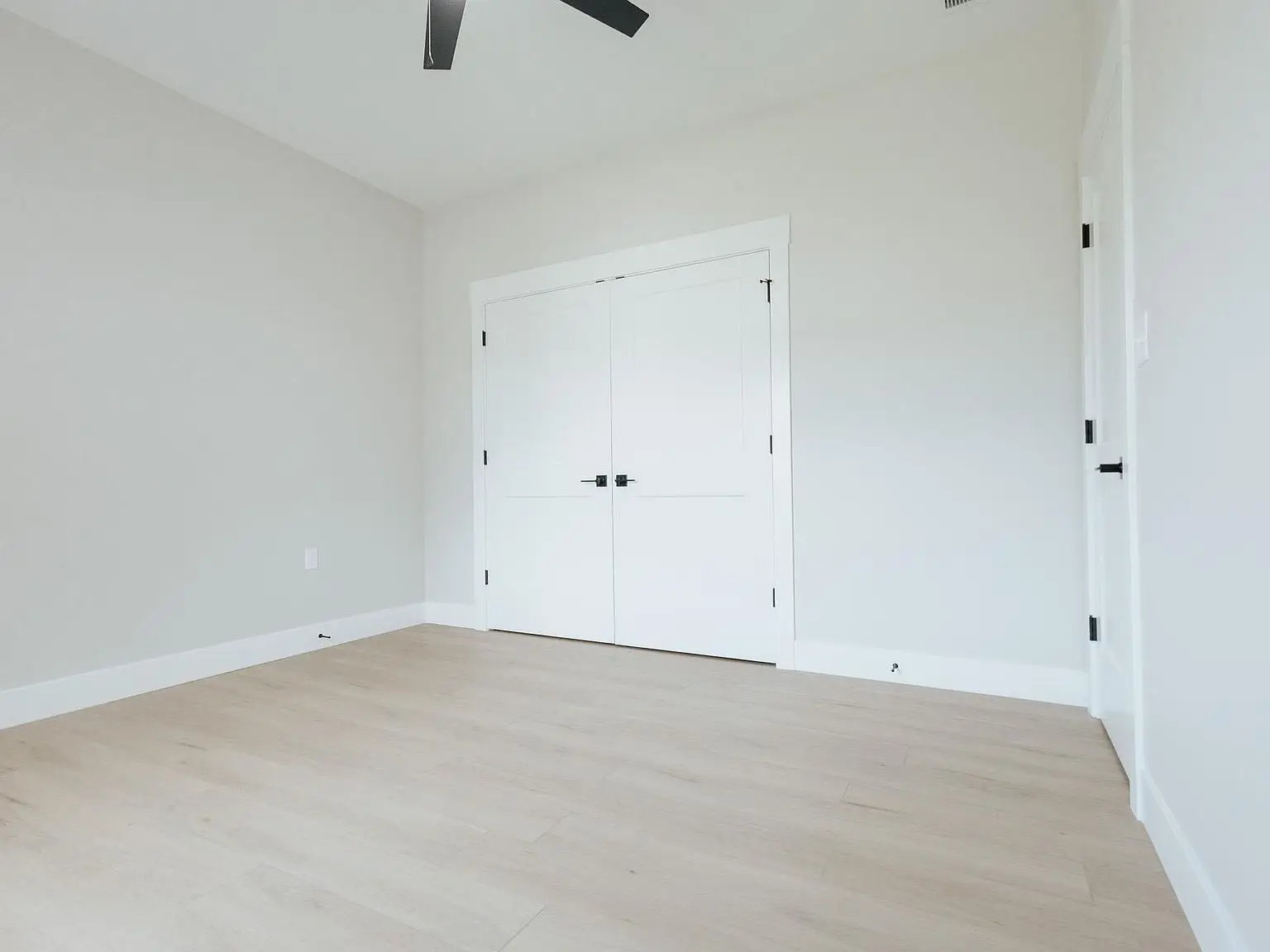 Empty room in the Harper home with light wood floor, white walls, and double closet doors.