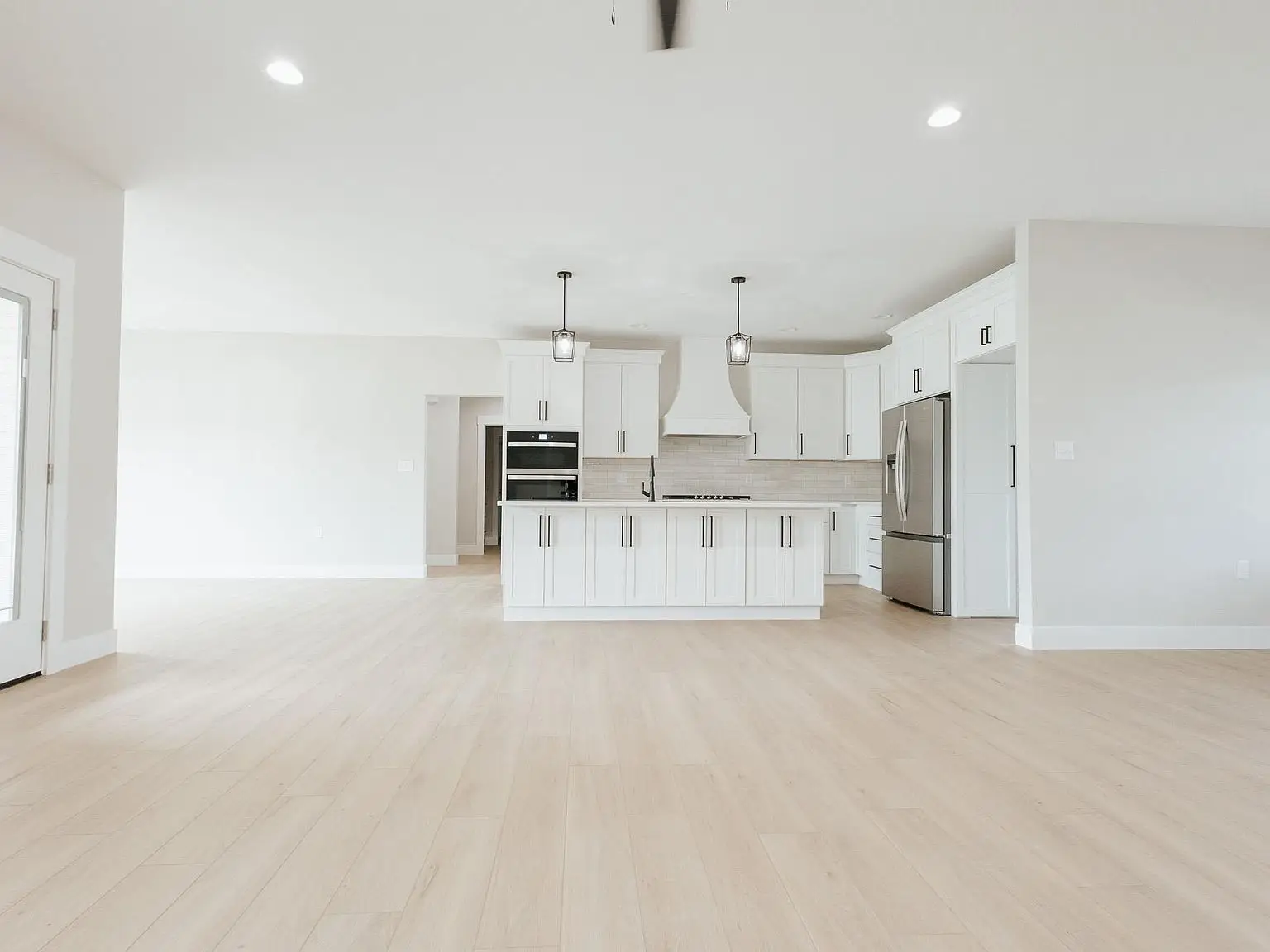 Modern, empty kitchen from the Harper floor plan with white cabinets, island, and wood flooring.