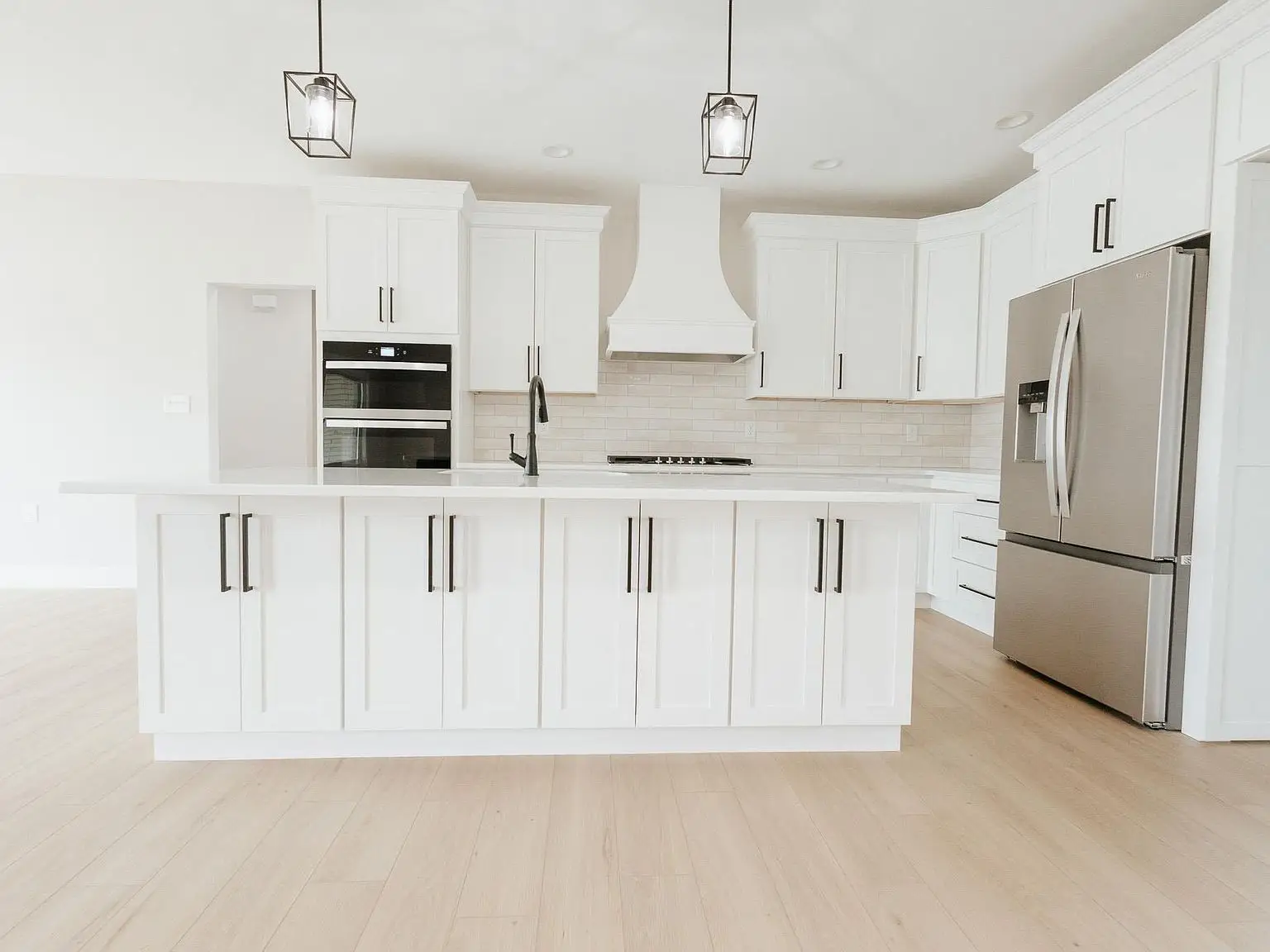 Modern white kitchen with island, Harper floor plan, stainless steel appliances, pendant lights.