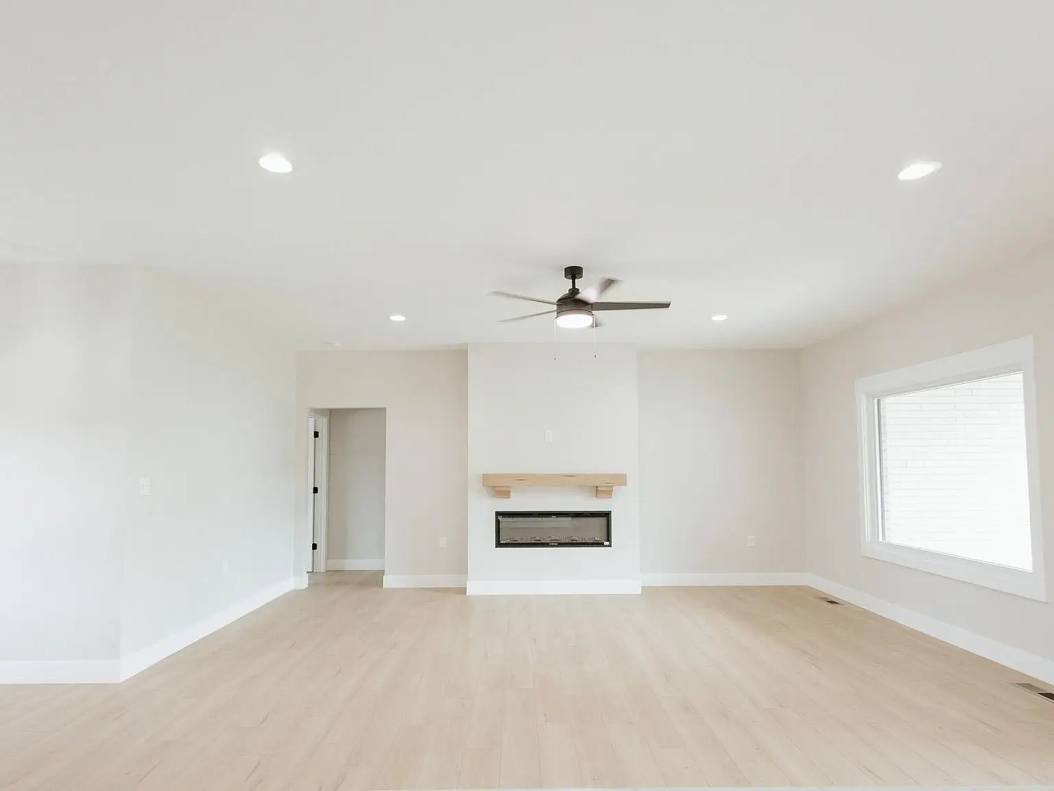 Empty Harper living room with light wood floor, fireplace, and large window on the right.