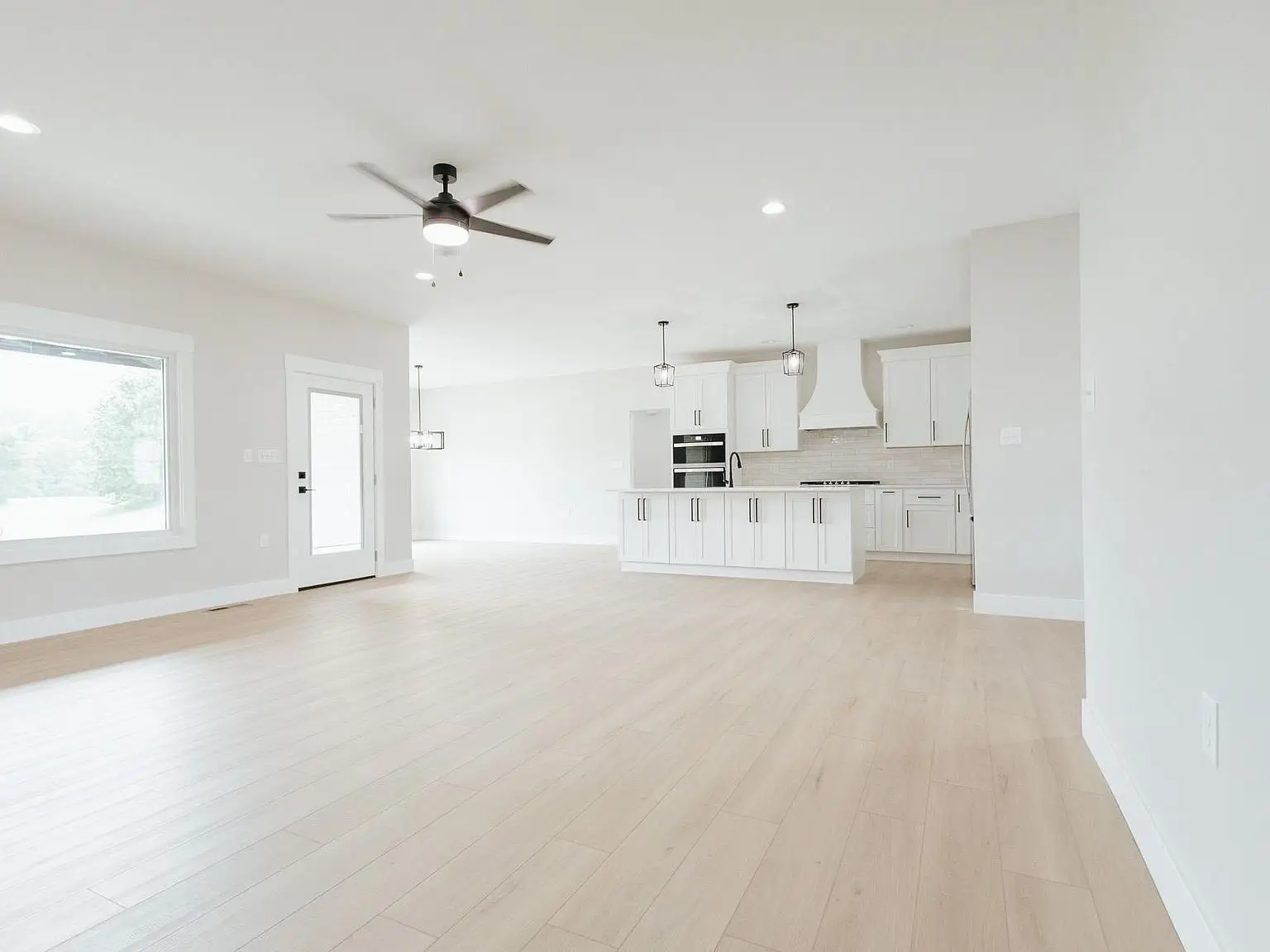 Spacious, empty room with light wood floors in the Harper home and a modern kitchen in back.