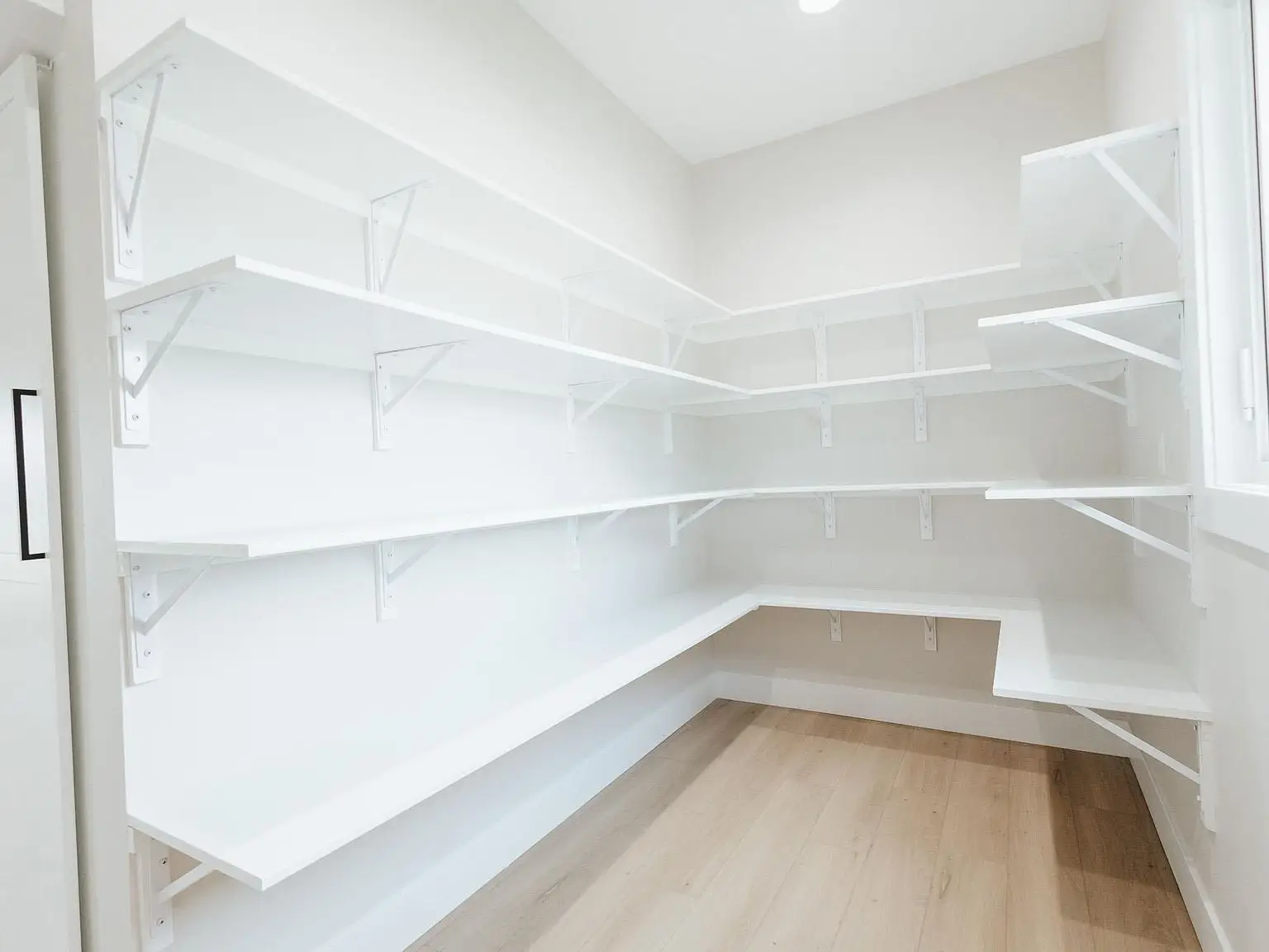 Empty walk-in pantry with white shelves and wood flooring in the Harper home by Chris Brown Homes.
