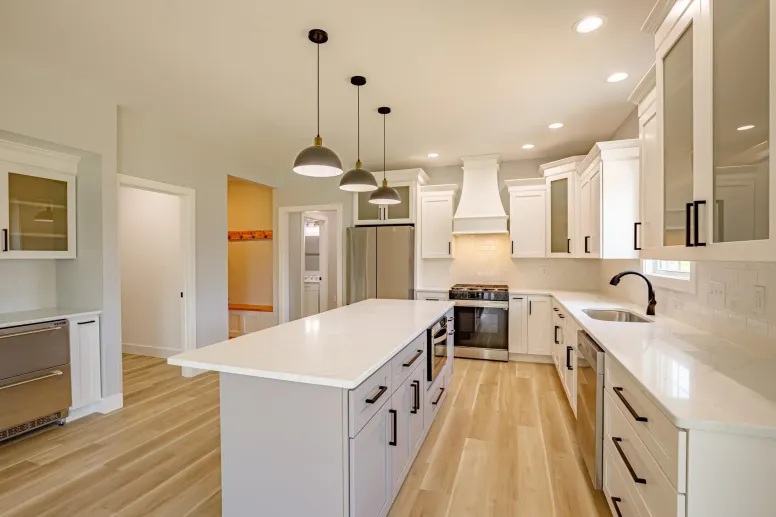 Modern kitchen with white cabinets, light wood floors, a large island, black pendant lights, stainless steel appliances, and bright recessed lighting—perfect inspiration for your next home decor blog.