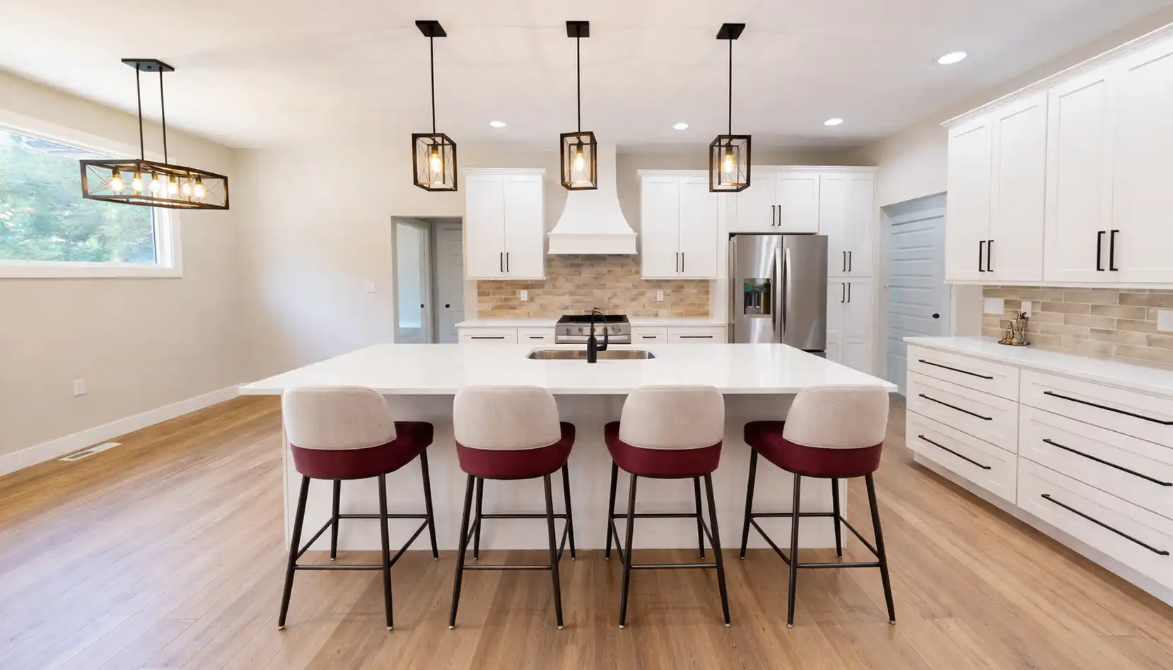 Modern Sophia kitchen with white cabinets, a large island with a white countertop, four chairs with red and beige upholstery, pendant lights above, stainless steel appliances, and wood flooring