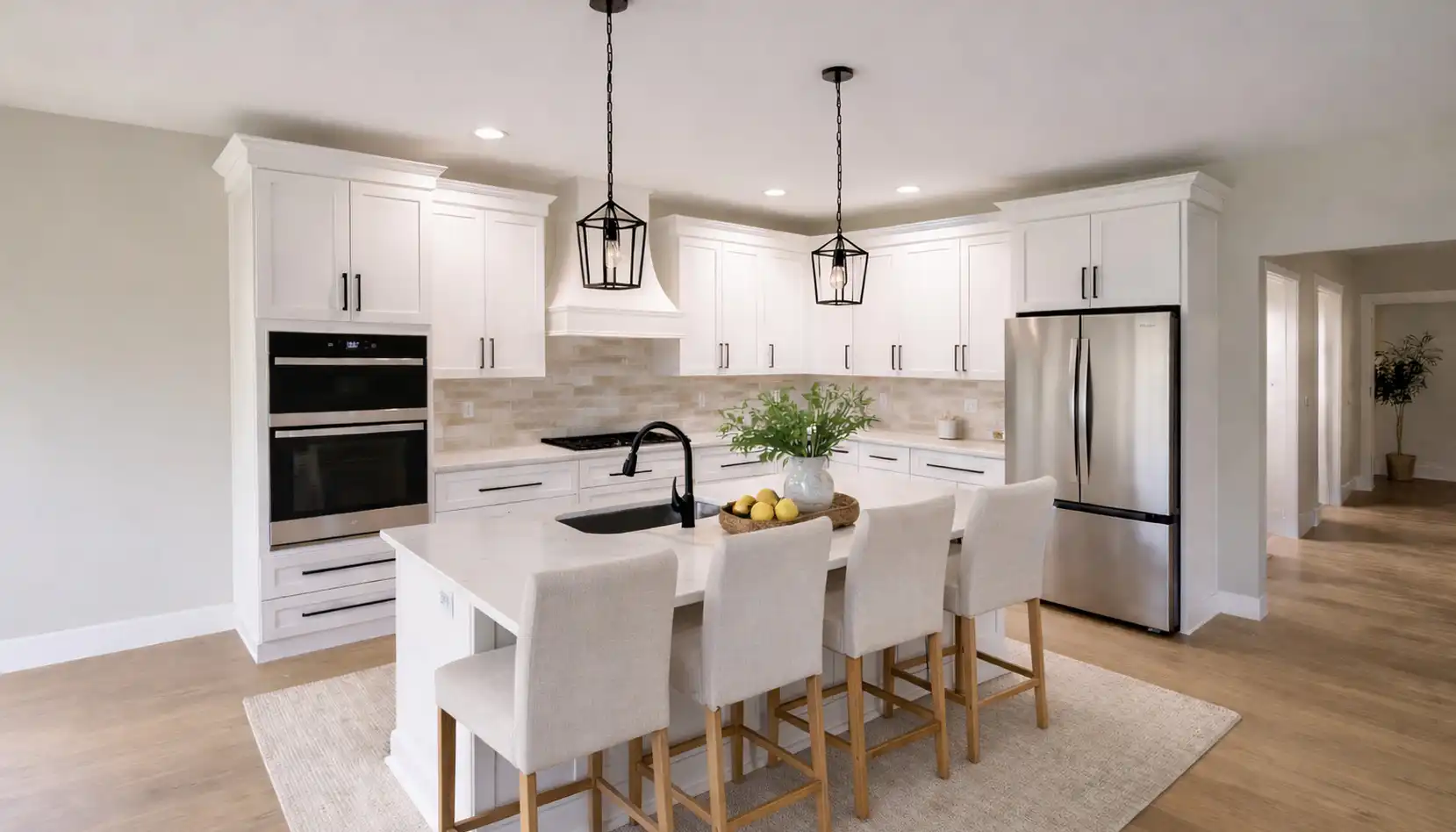 Modern kitchen with white cabinets, stainless steel appliances, island with sink, four upholstered chairs, pendant lights, a bowl of lemons, and a vase of greenery on the island—plus a subtle robin’s egg blue accent lending a fresh touch. Light wood floors and neutral decor complete the inviting space