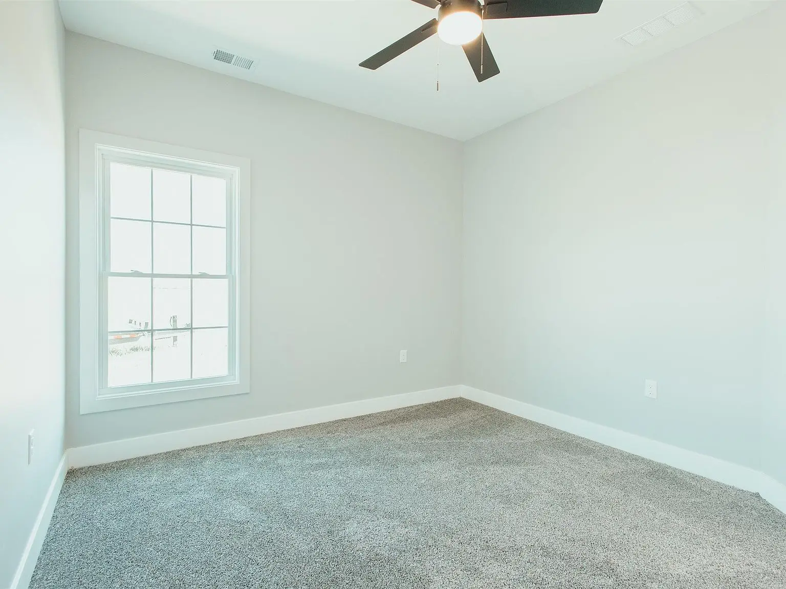 Empty room in Kirkwood floor plan with gray carpet, white walls, window, and ceiling fan.