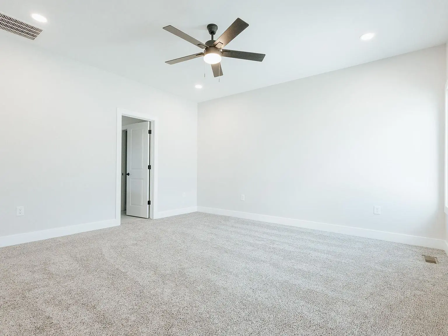 Empty, carpeted room at Chris Brown Homes 18801 Roscommon Rd with a ceiling fan and open door.