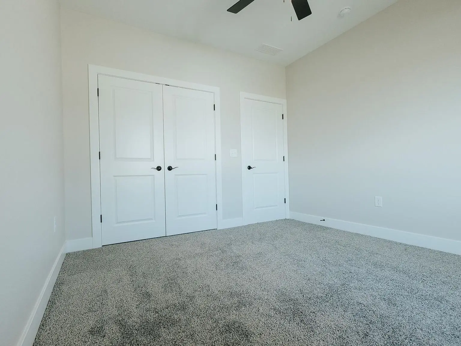 Empty room in the Asher floor plan with beige walls, gray carpet, and two closed white doors.