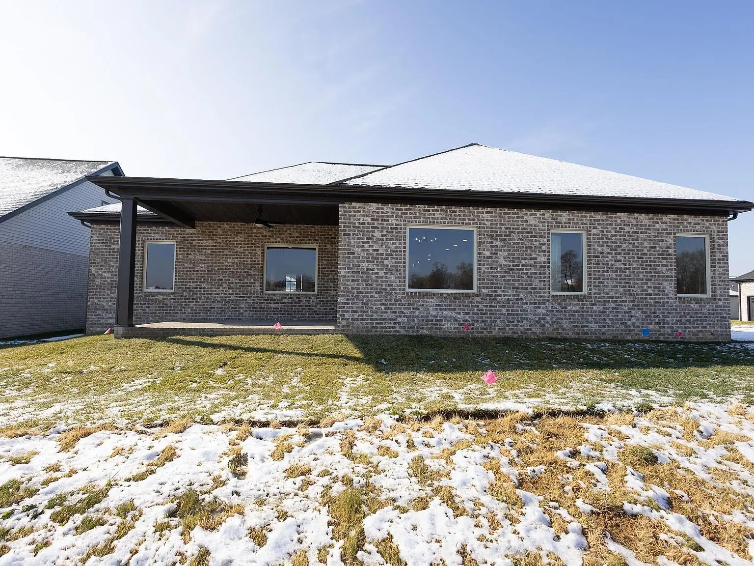 Asher floor plan brick house with four windows, covered patio, and patchy snow in front.